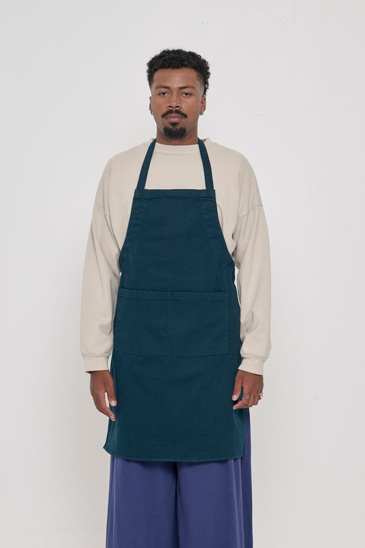 Front view of a person in an Adjustable Apron in Juniper, with straps tied behind their back.