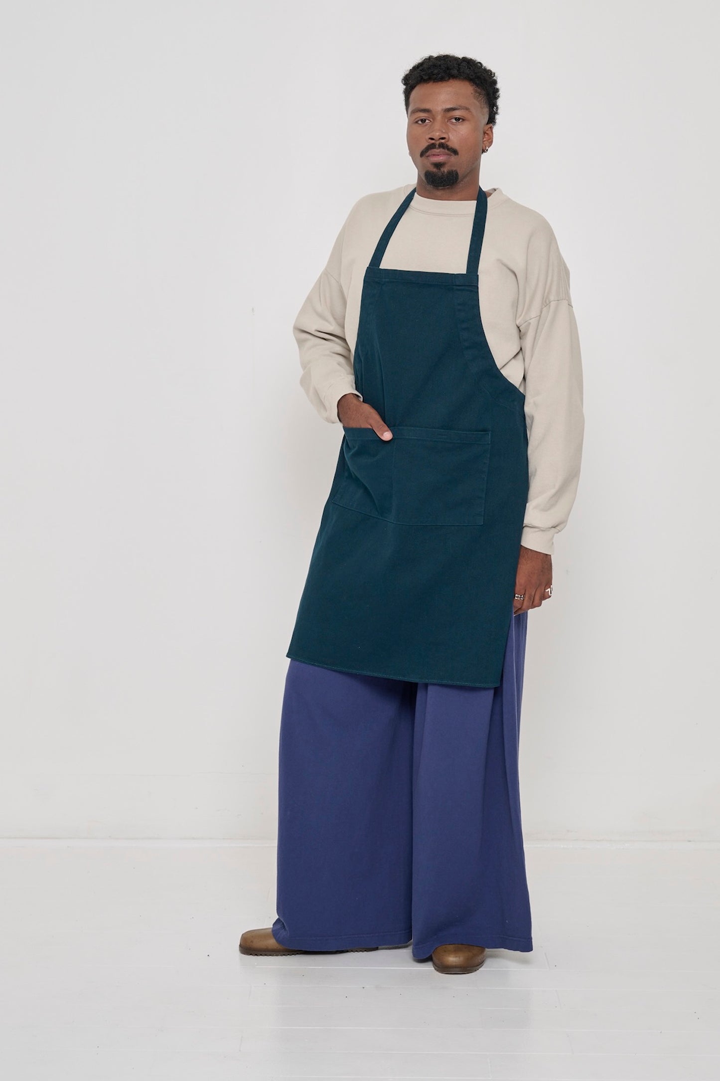 Juniper Adjustable Apron on a man, covering chest to knees, one hand in large front pocket.