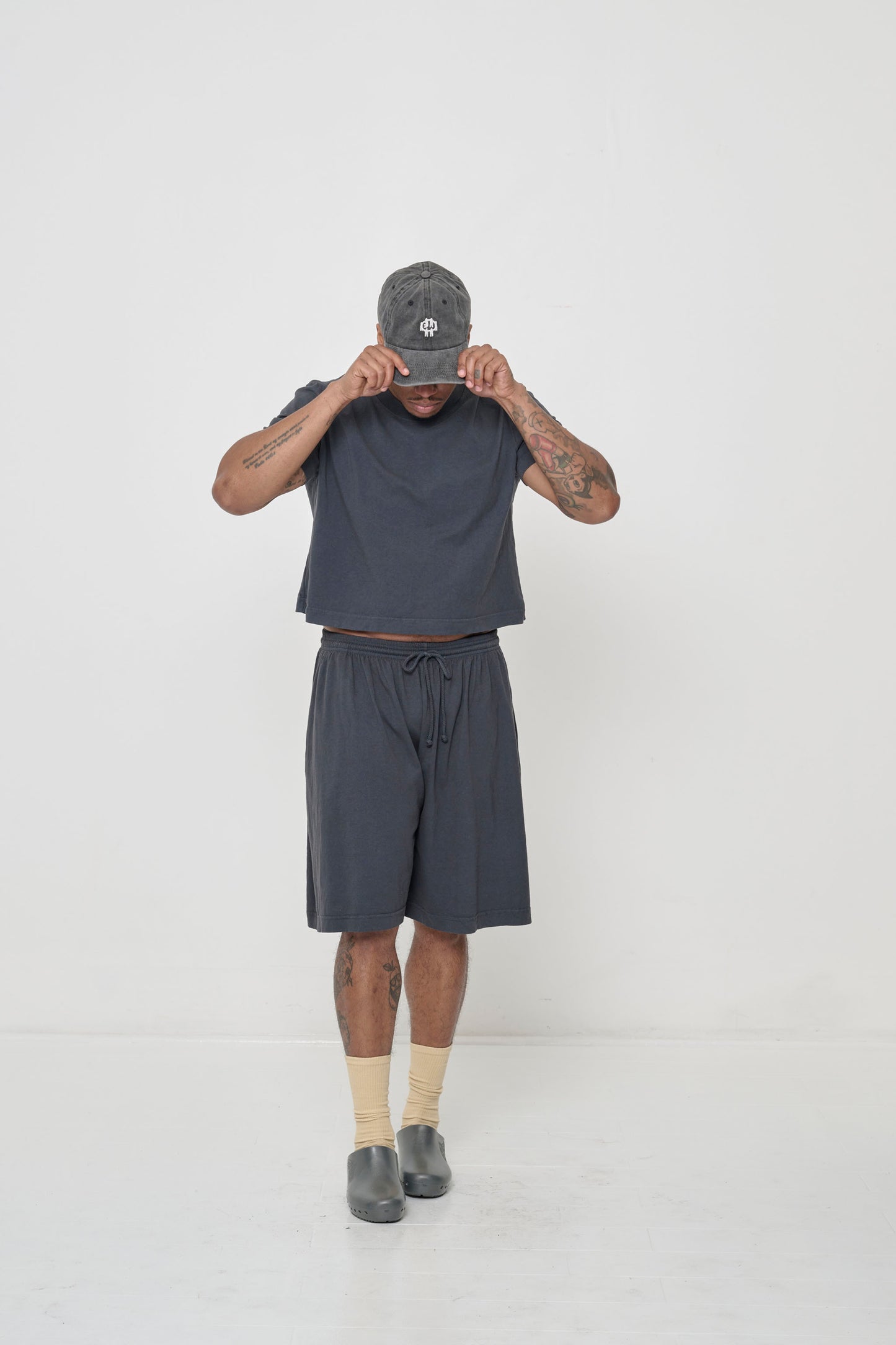 Hands raised to Bucky Logo Cap bill, lifting shirt hem to show a sliver of navel.