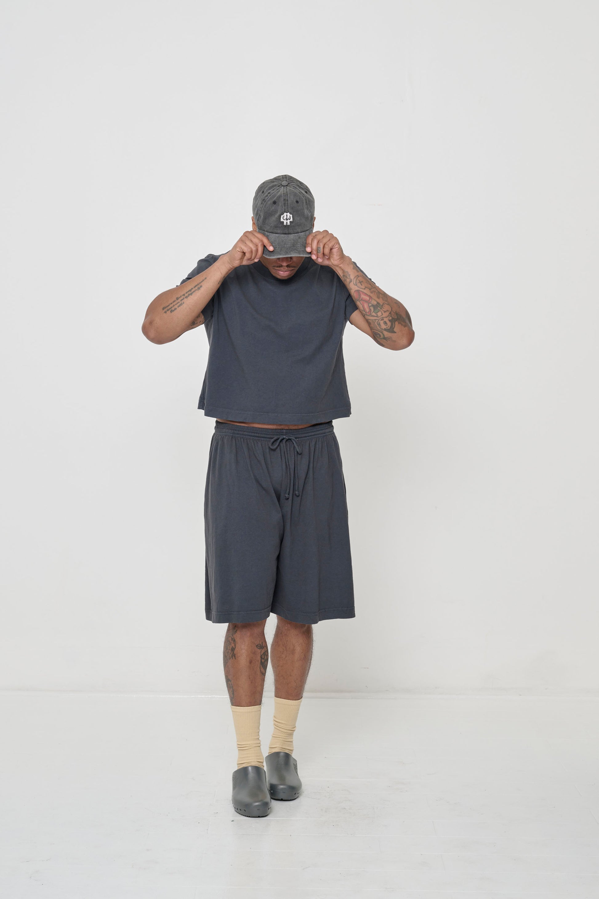 Hands raised to Bucky Logo Cap bill, lifting shirt hem to show a sliver of navel.