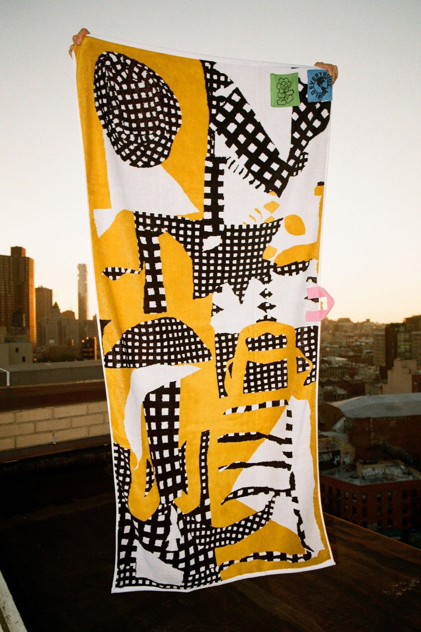 Person holding up a yellow, black, and white abstract patterned towel to display its full design.
