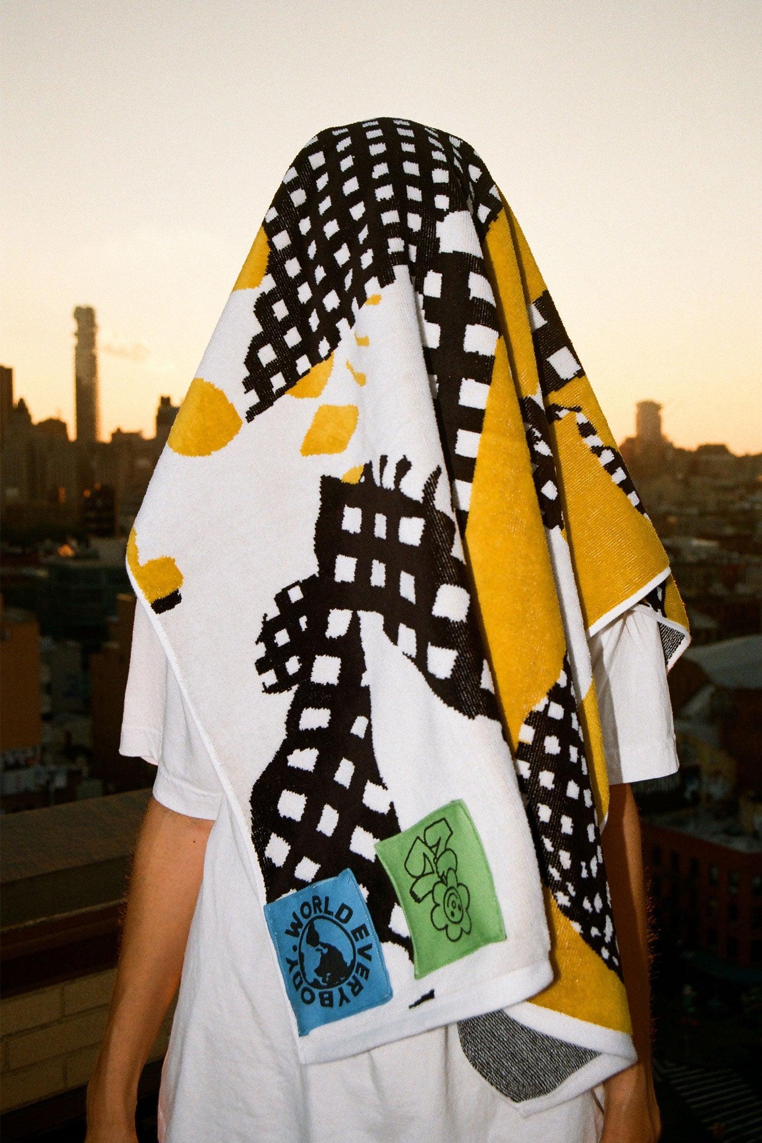 Towel draped over a person's head, standing with a city skyline in the background