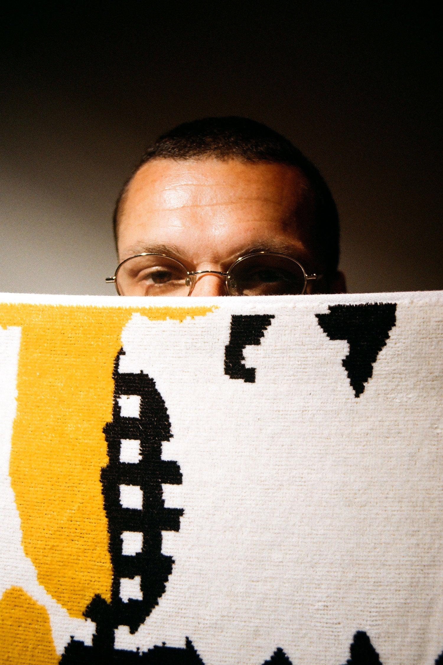 Close up of Braulio Amado peering over an edge of the towel, showing textured towel fabric.
