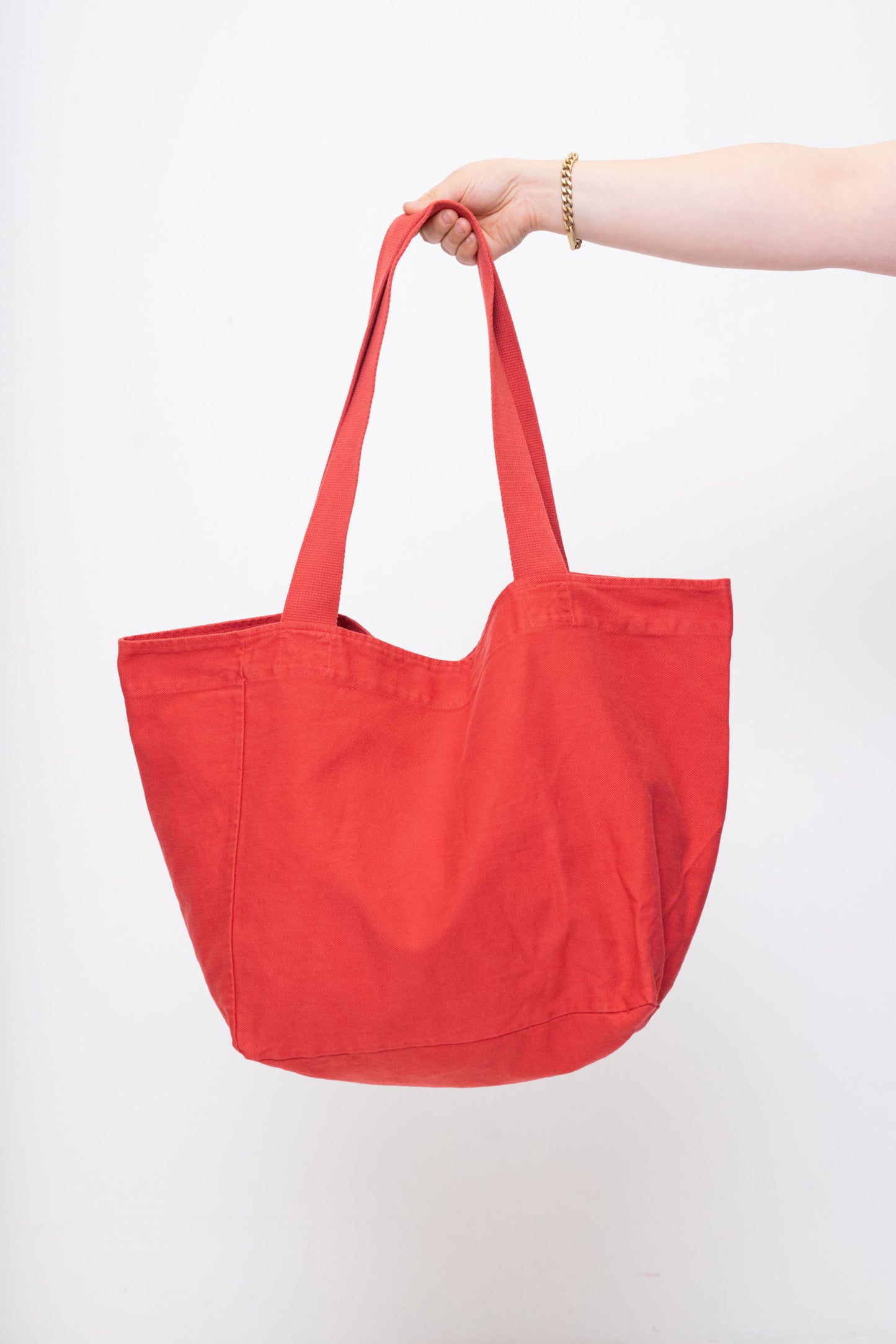 Big Tote in Cedar orange-red, held in a person's hand, showing gussets, depth, stitching, and web straps.
