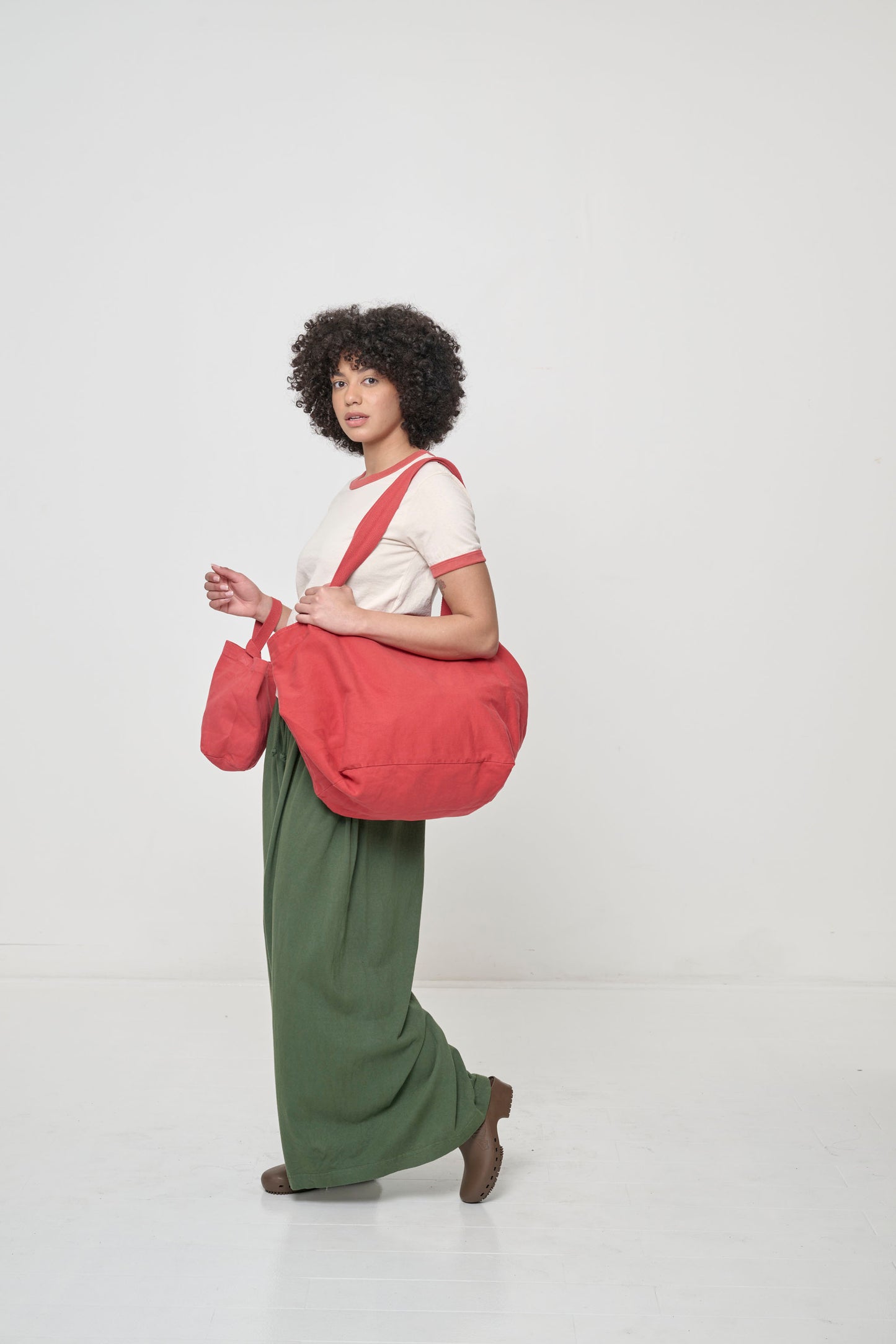 Woman holding Big Tote in Cedar orange-red on her shoulder, tilting the bag up to show the deep bottom panel.