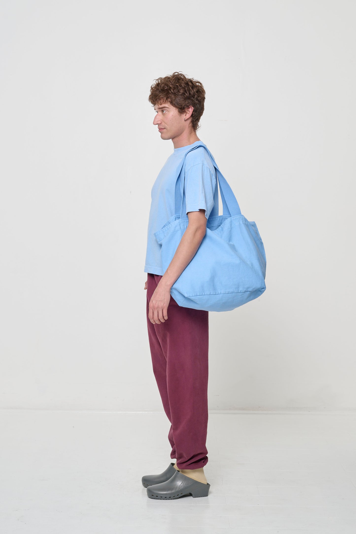 Person holding Big Tote in Cielo light blue on their shoulder, showing that straps end and the bag opening begin at their mid-torso.