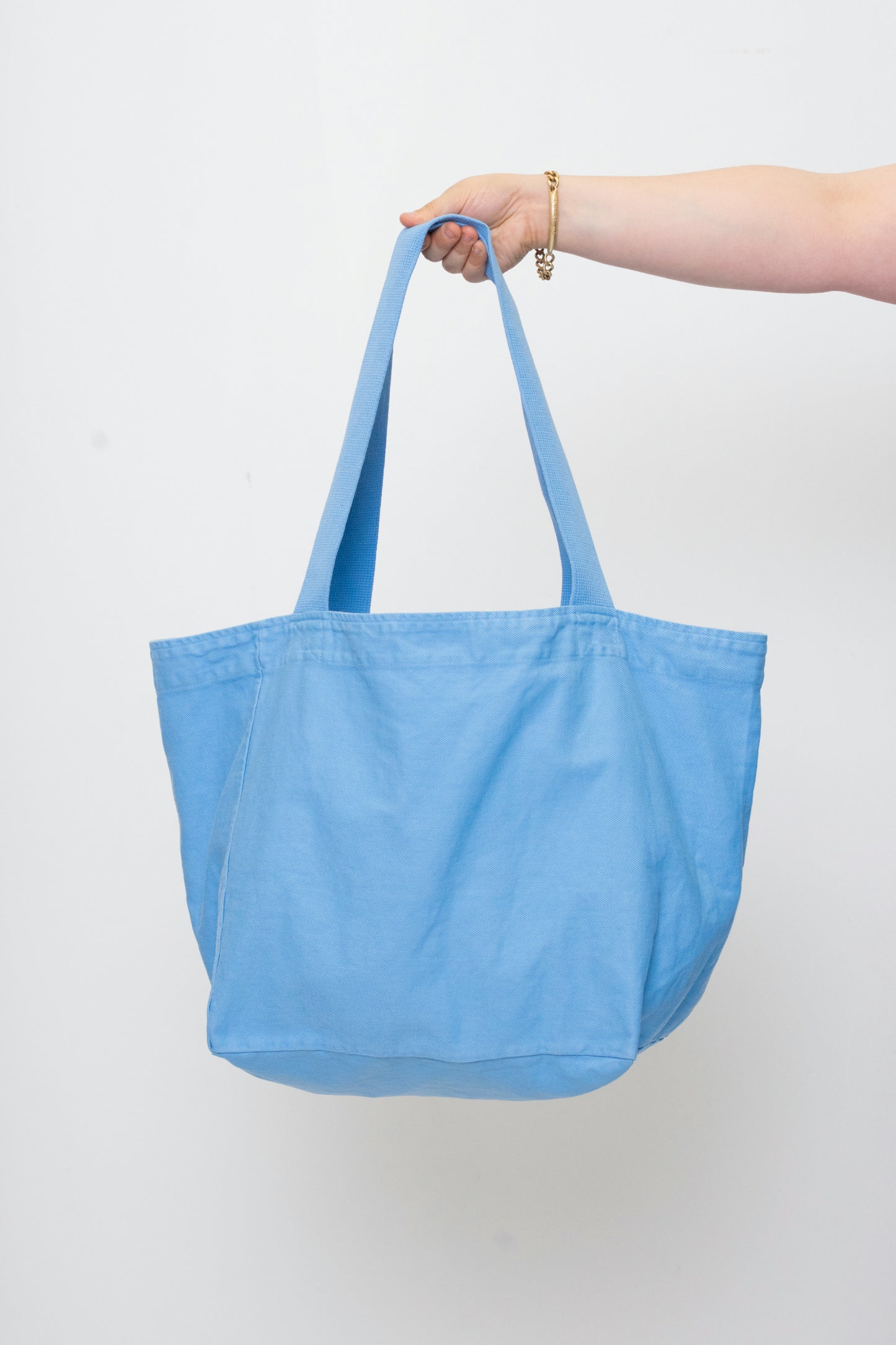 Big Tote in Cielo light blue, held in a person's hand, showing gussets, depth, stitching, and web straps.