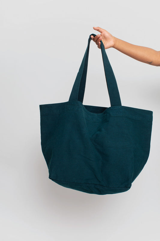 Big Tote in Juniper dark blue-green, held in a person's hand, showing gussets, depth, stitching, and web straps.