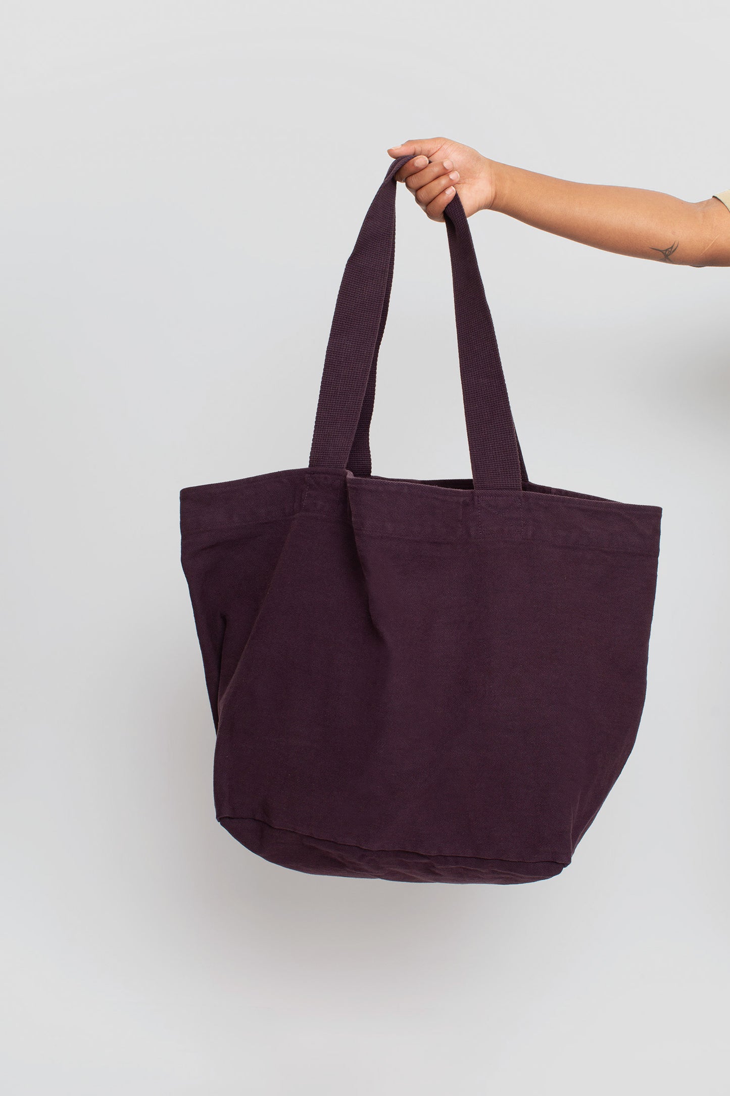 Big Tote in Mulberry dark purple, held in a person's hand, showing gussets, depth, stitching, and web straps.
