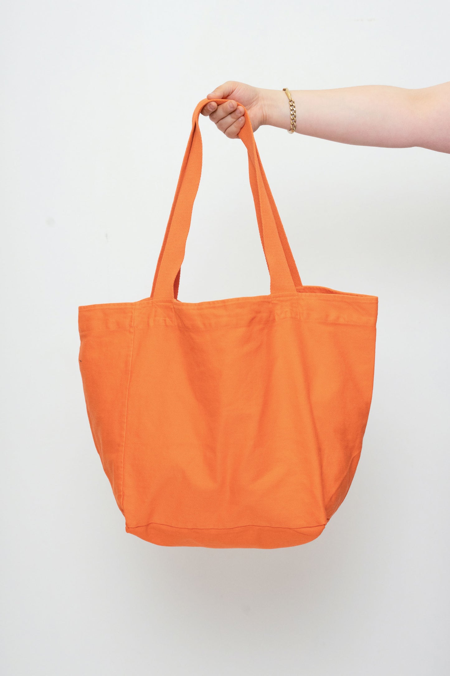 Big Tote in Persimmon orange, held in a person's hand, showing gussets, depth, stitching, and web straps.