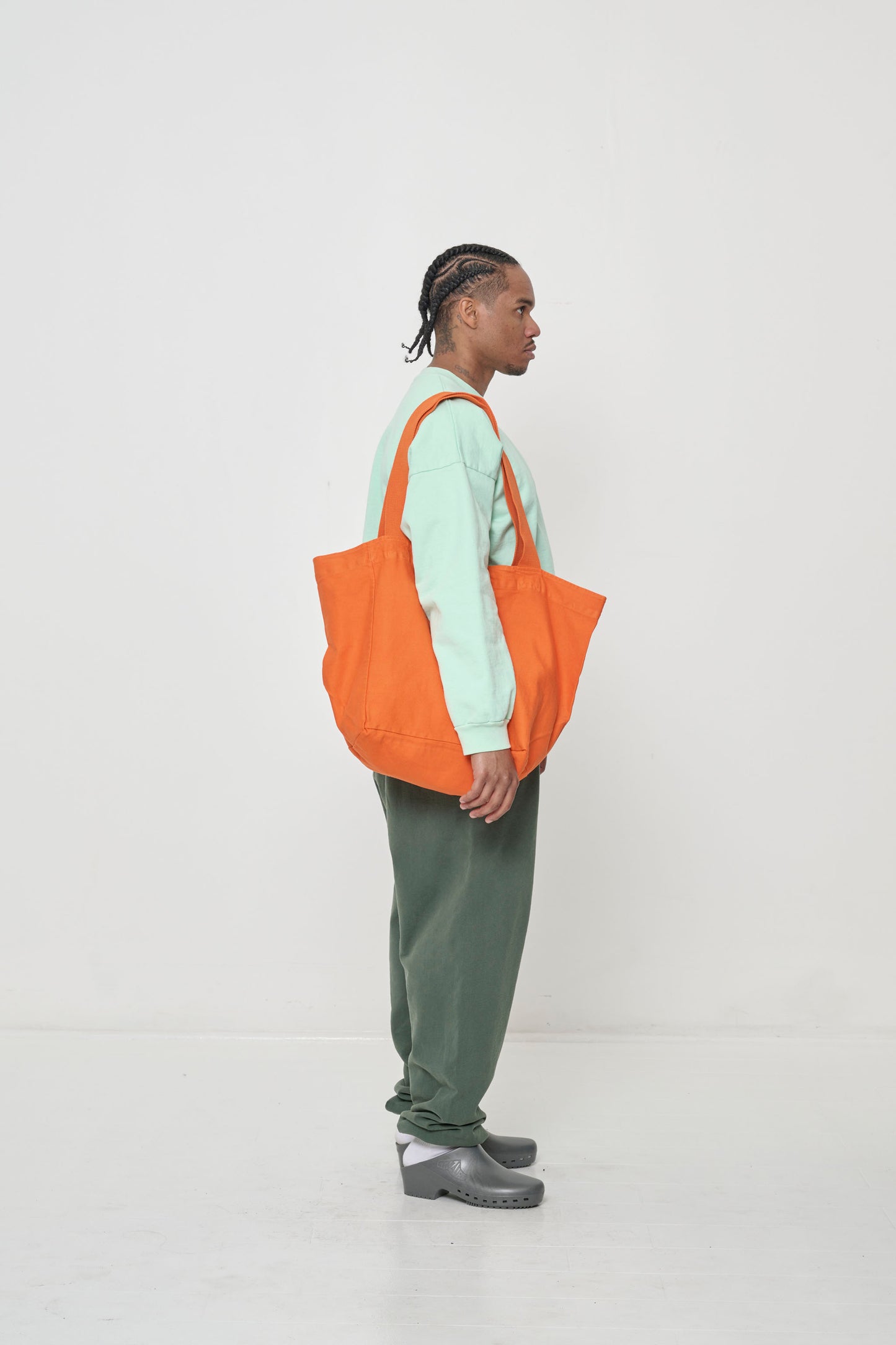 Profile of man holding Big Tote in Persimmon orange and the length of the bag is wider than the side silhouette of his body.