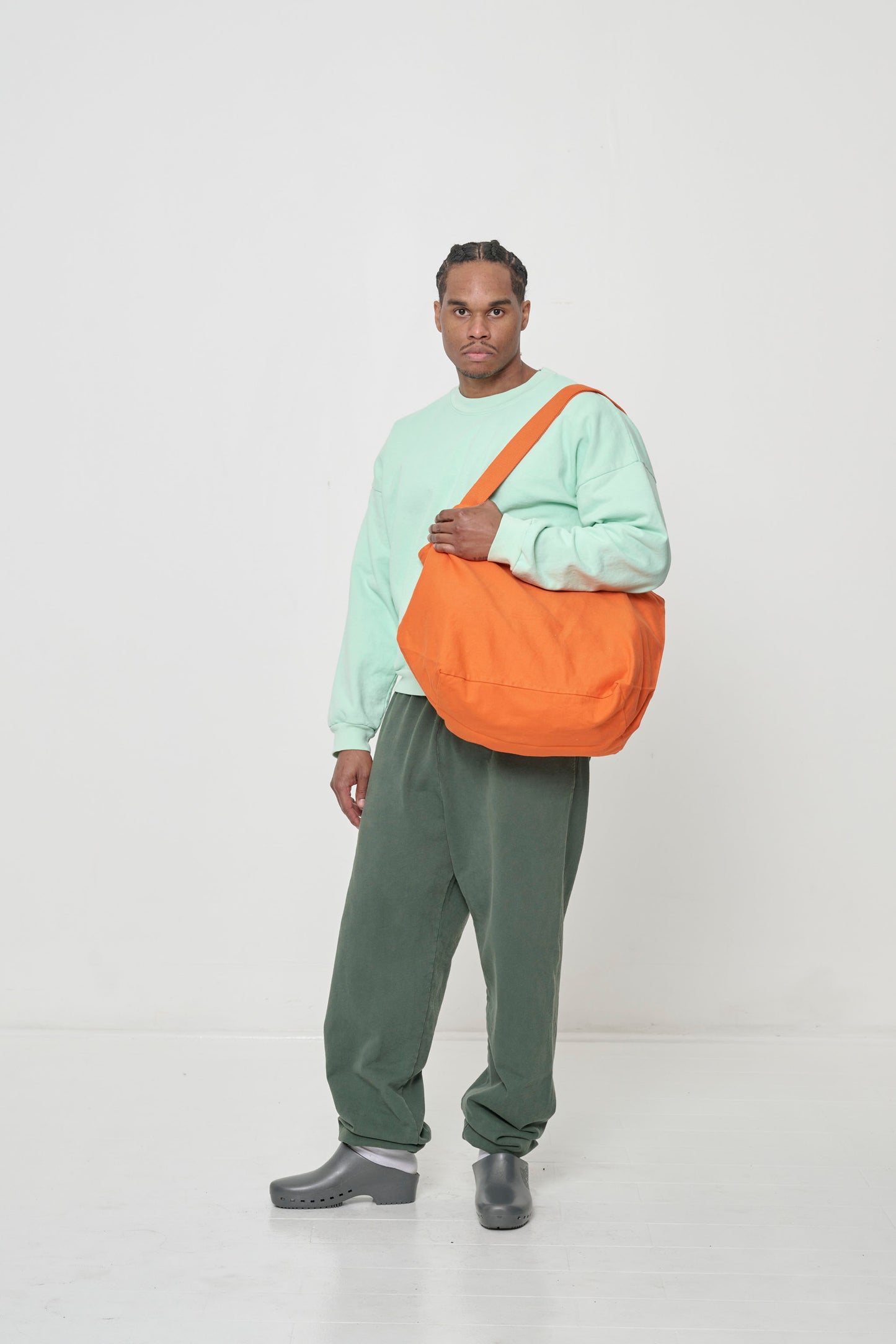 Man holding Big Tote in Persimmon orange on his shoulder, showing that the bag opening is even to his mid-torso.