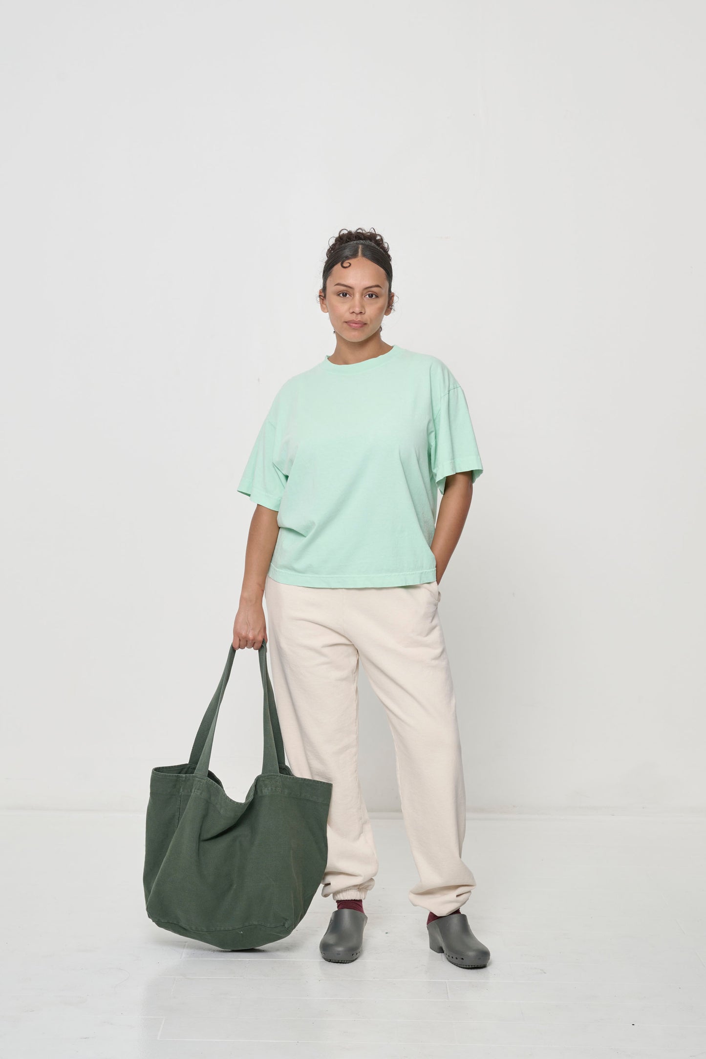Woman holding Big Tote in Pine greyish dark green over in her hand, showing how the fabric is flexible yet sturdy.