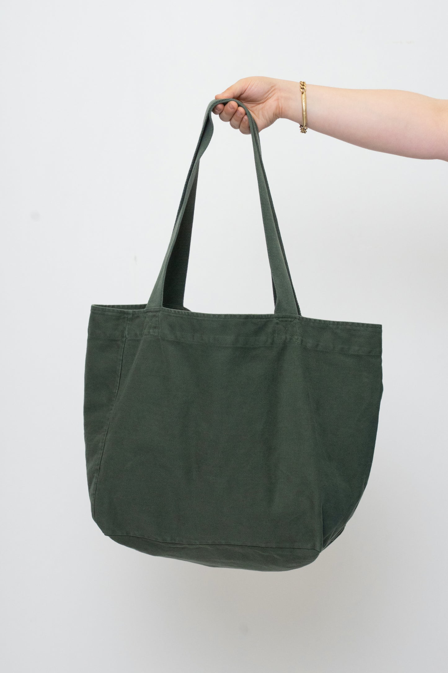 Big Tote in Pine greyish dark green, held in a person's hand, showing gussets, depth, stitching, and web straps.