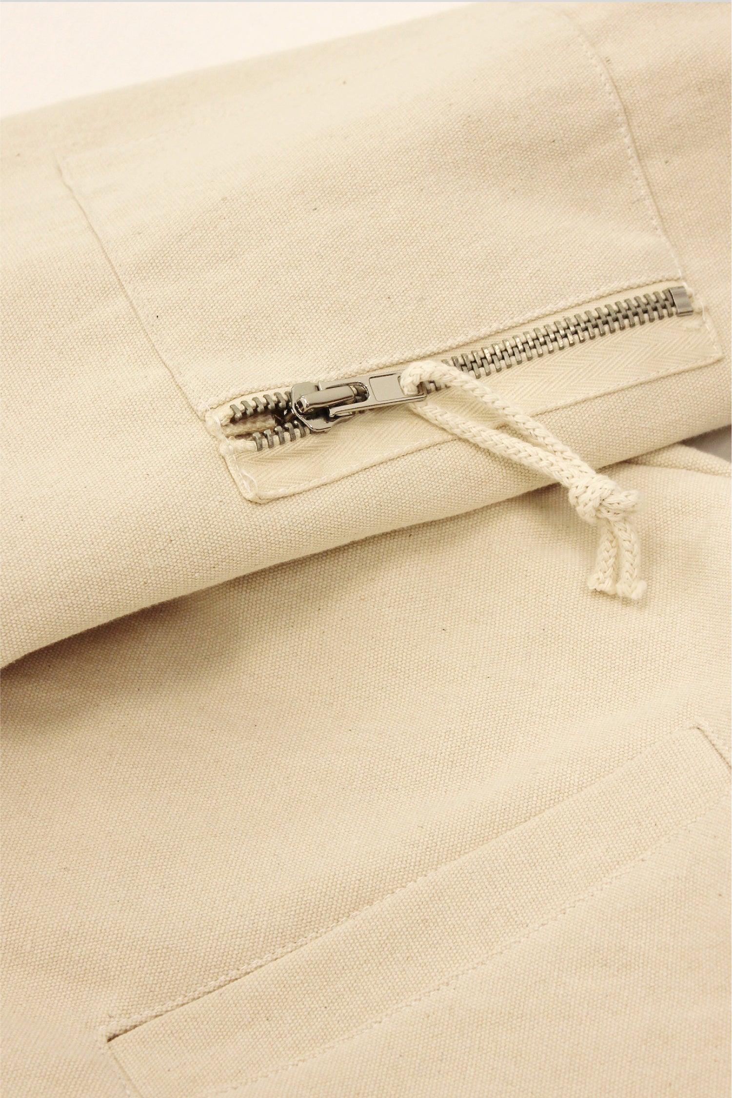 Close up flat lay of the Biodegradable Bomber Jacket in Natural, showing details of the upper arm pocket and metal zip closure.