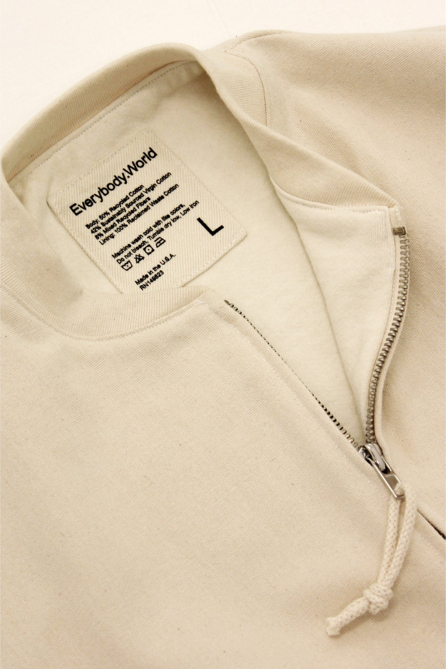 Close up flat lay of the Biodegradable Bomber Jacket in Natural, showing the details of the inside back patch label and front metal zip.