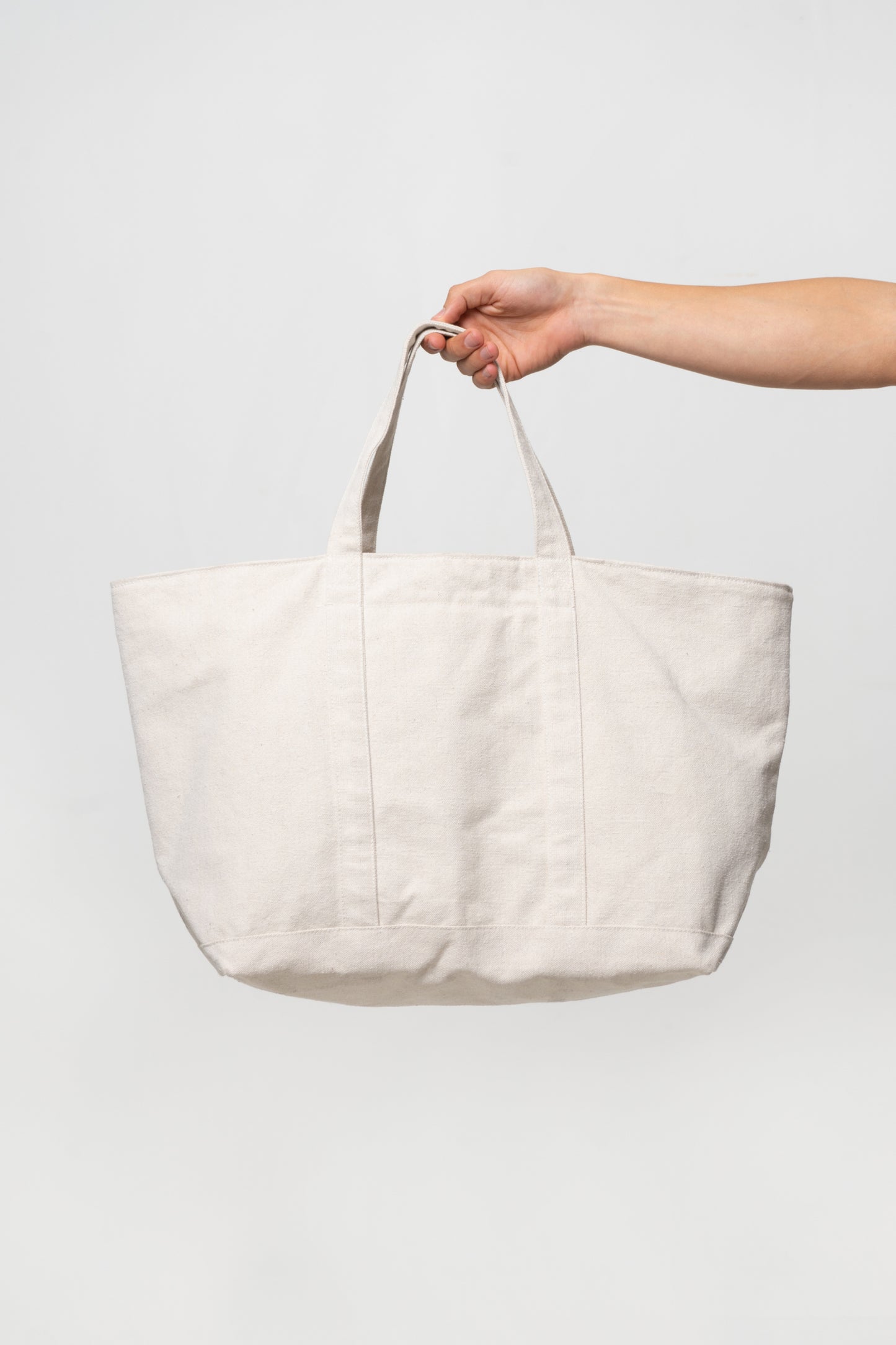 Overnight Tote in Natural, held in a person's hand, showing web straps, and "back" side without the exterior pocket.