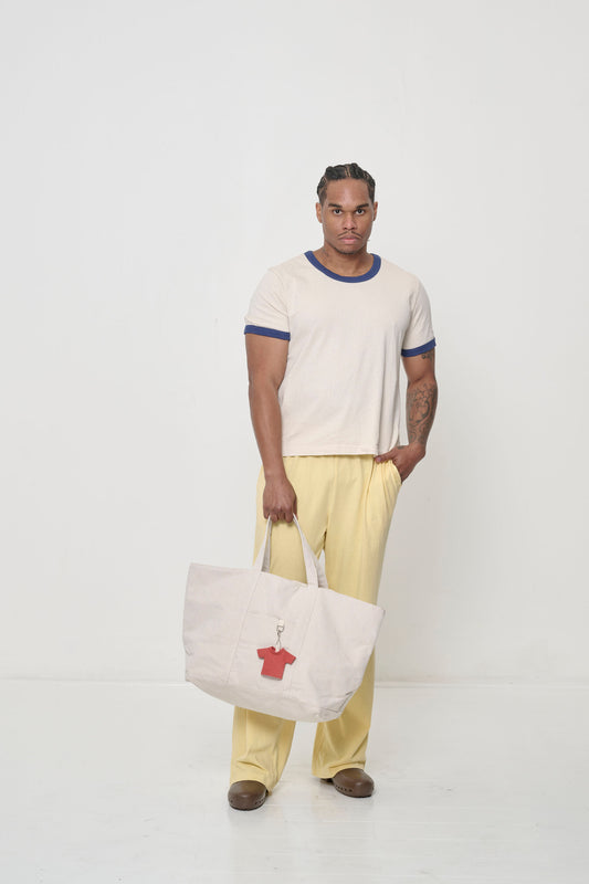 A man wearing a Ringer Trash Tee and yellow Apartment Pants, holding the bag in his hand.