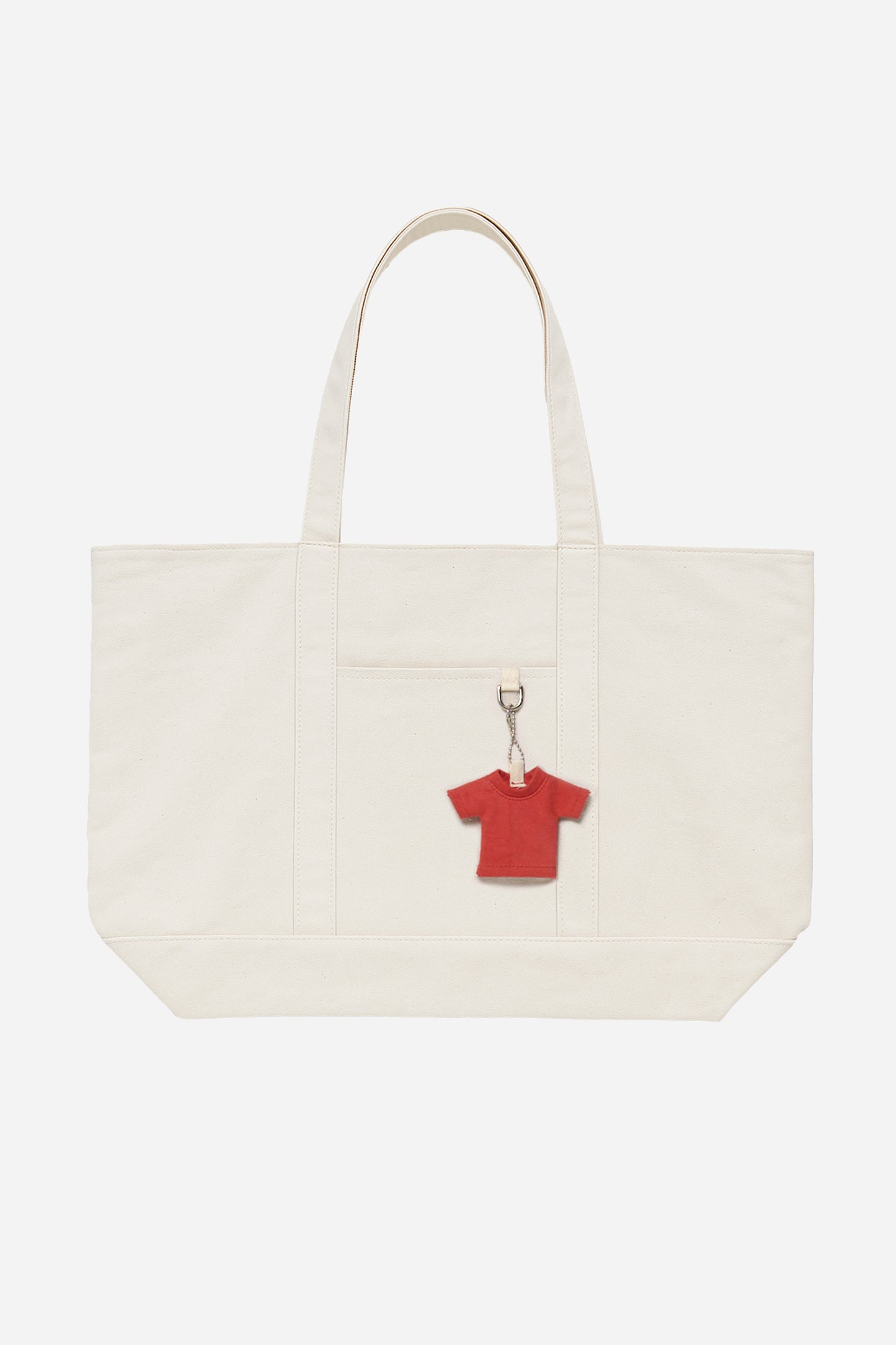 Flat lay of Overnight Tote in Natural, shows straps, bottom panel, stitching, exterior pocket, and red mini Trash Tee charm.