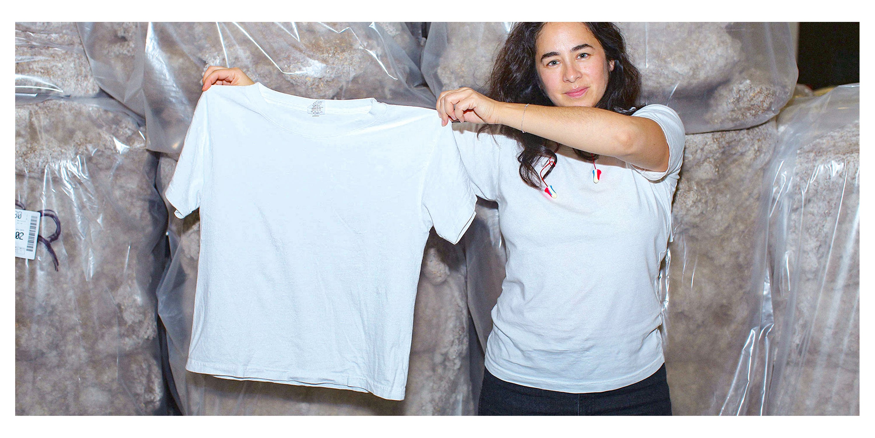 Carolina Crespo, Everybody.World co-founder, holding up a Trash Tee and standing in front of bags of cotton.
