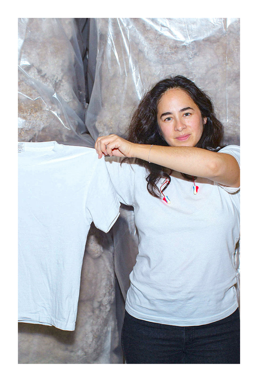 Carolina Crespo, Everybody.World co-founder, holding up a Trash Tee and standing in front of bags of cotton.