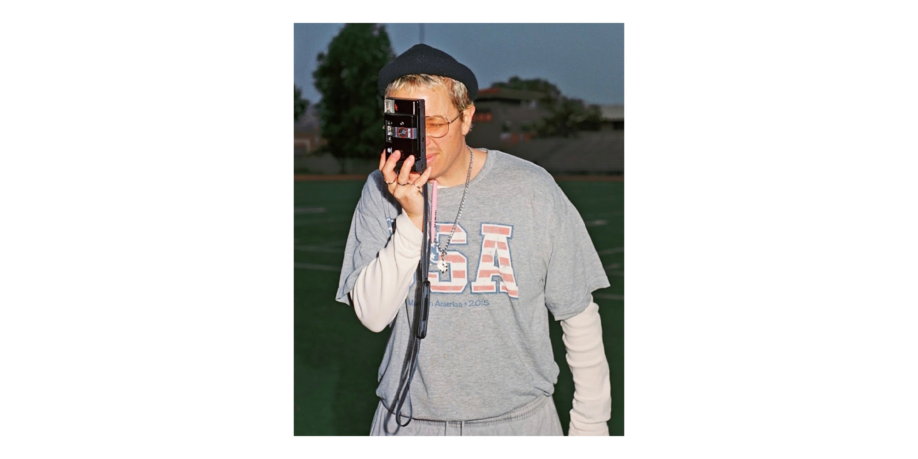 Ariel outside on an athletic field, holding a camera up to his face.