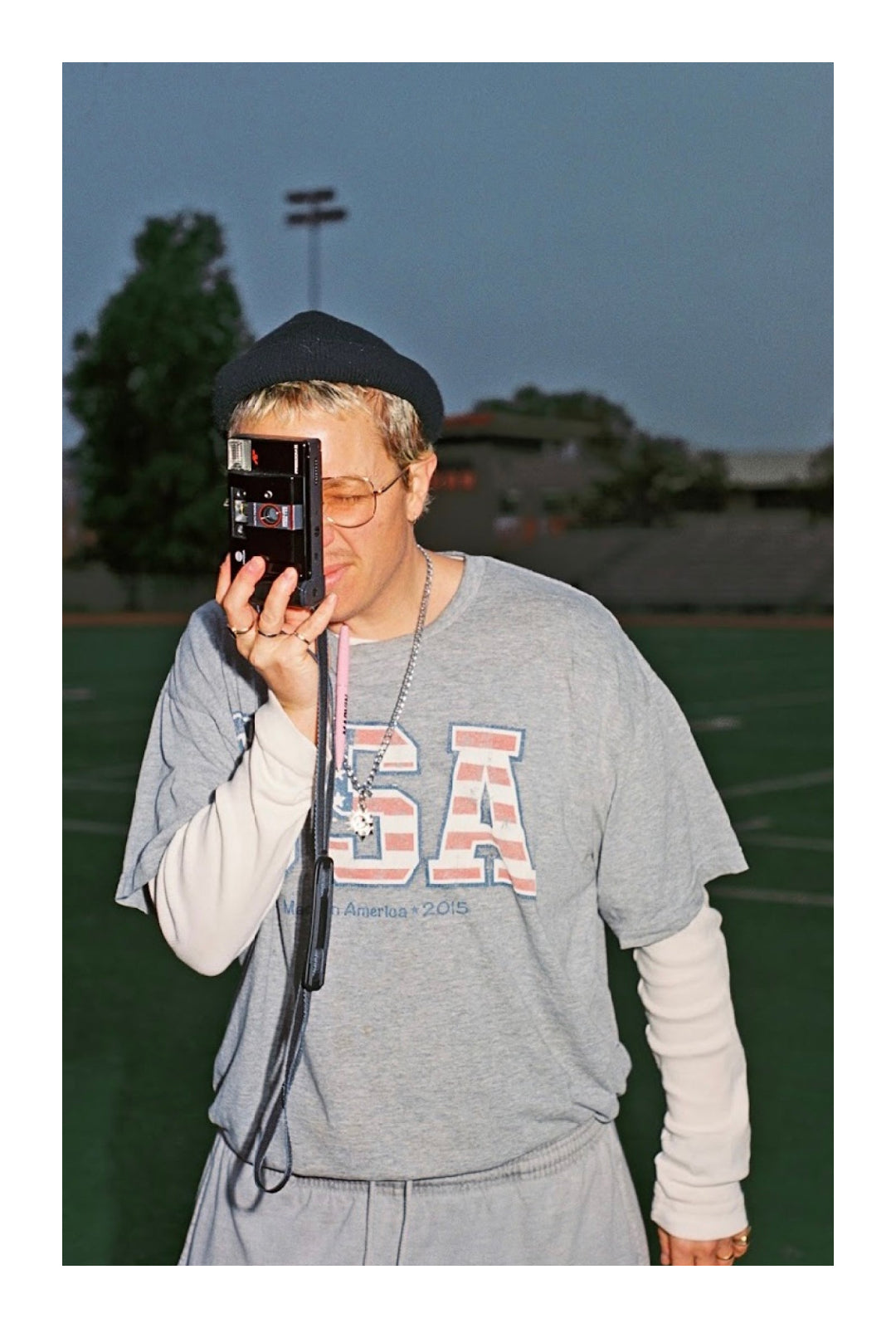 Ariel outside on an athletic field, holding a camera up to his face.