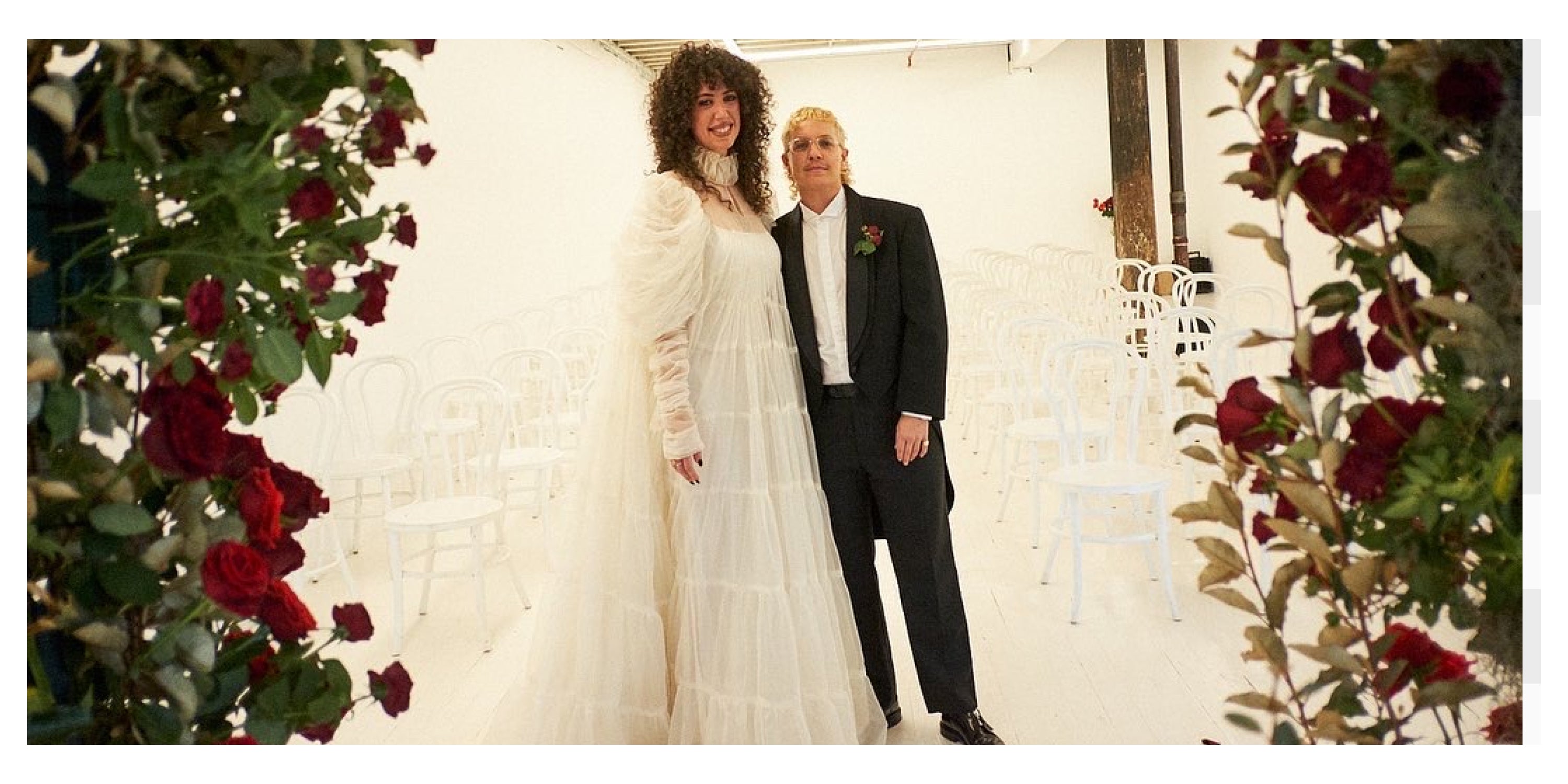 Jerico in wedding dress and Ariel in a tux, in front of rows of white chairs and roses on each side of frame.
