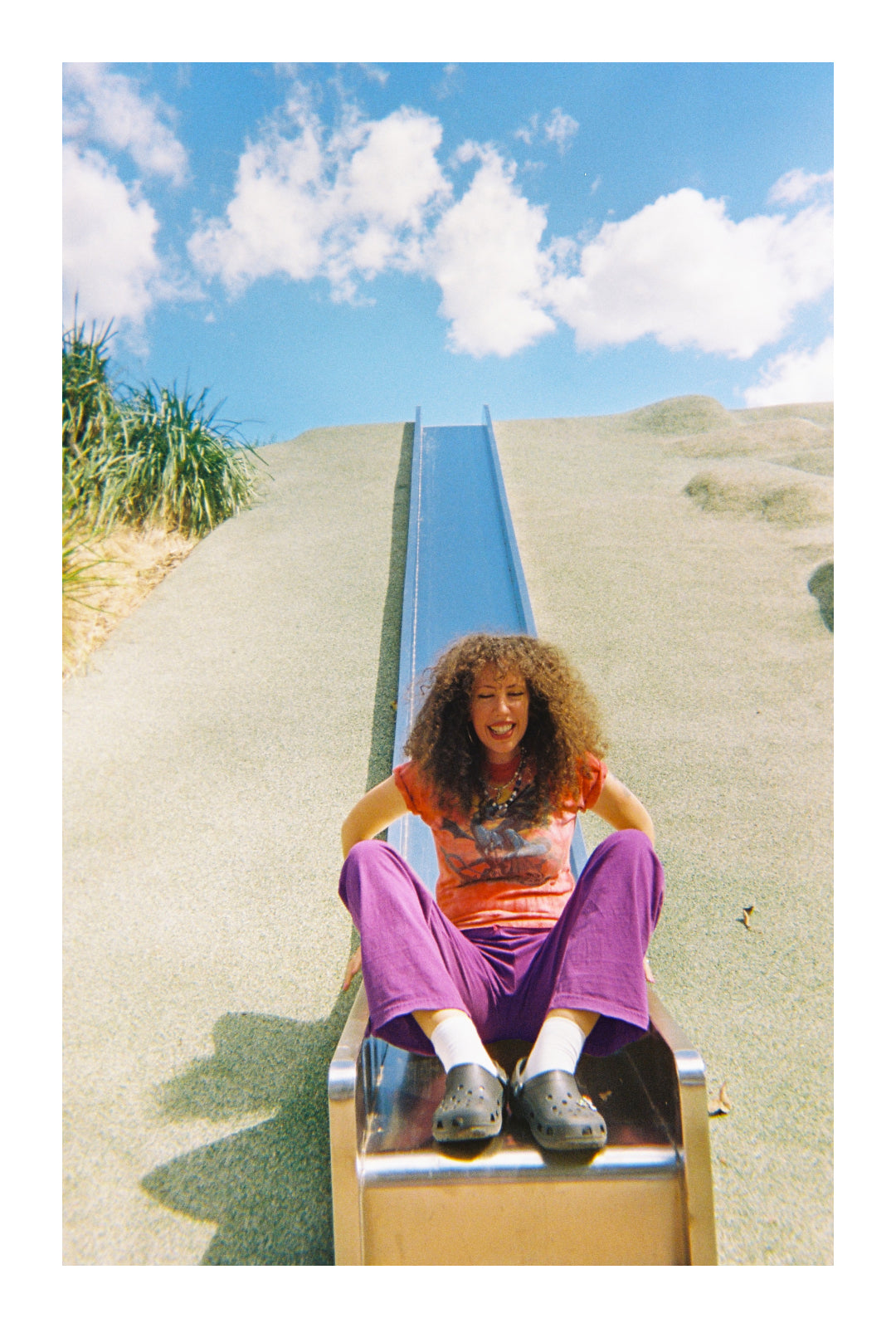 Jerico in a red graphic tee and purple Apartment Pants, at the bottom of a metallic park slide.