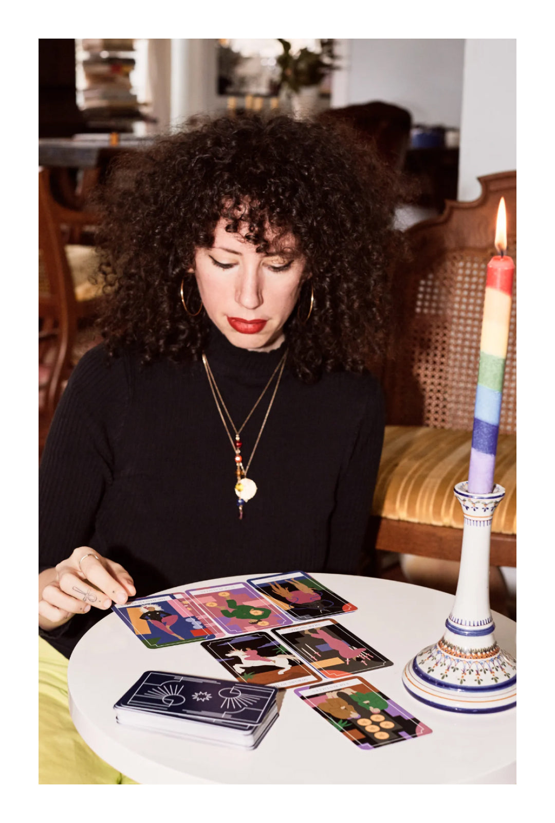 Jerico reading tarot cards at a small round table. A rainbow candlestick is lit.