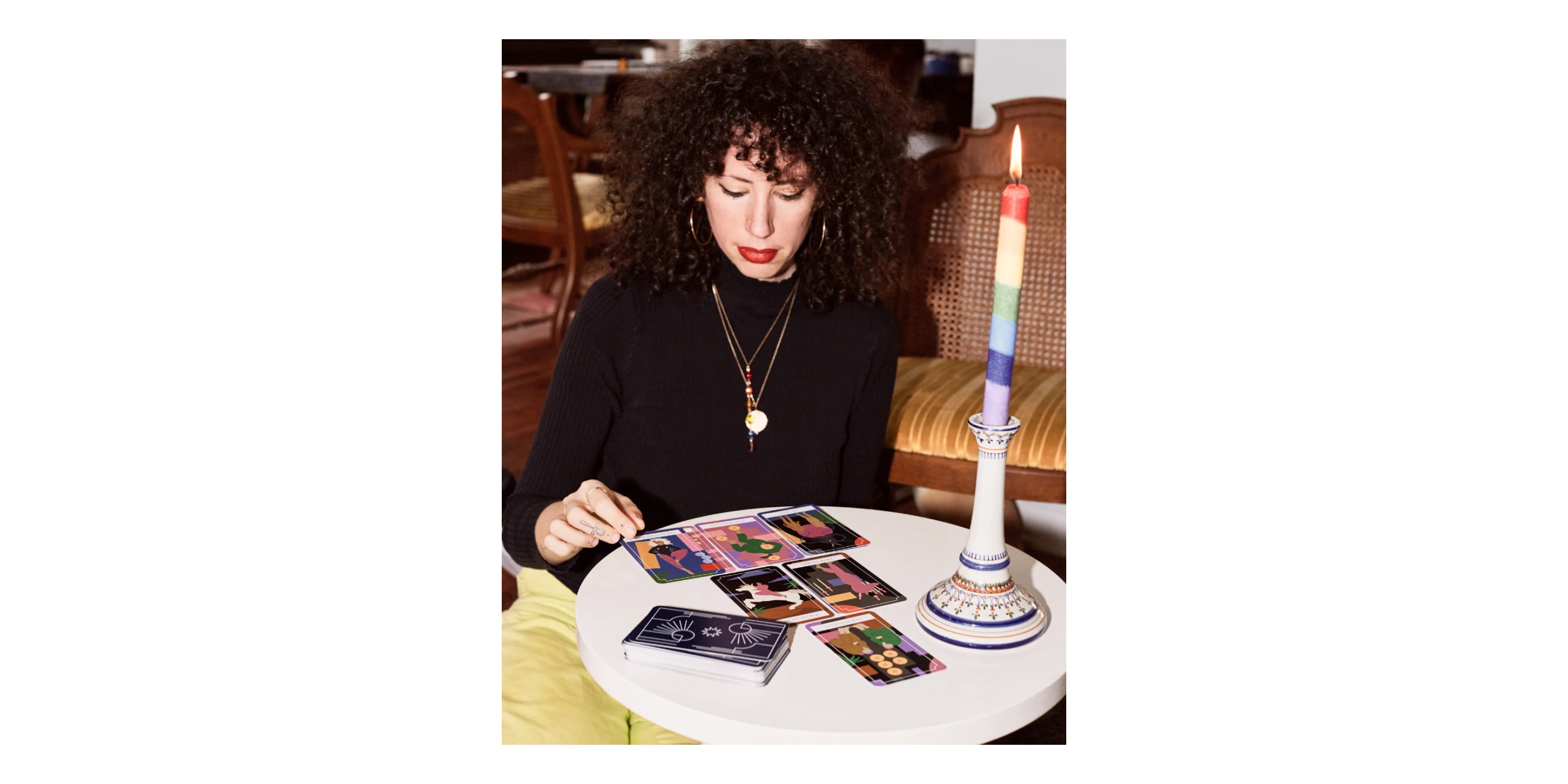 Jerico reading tarot cards at a small round table. A rainbow candlestick is lit.