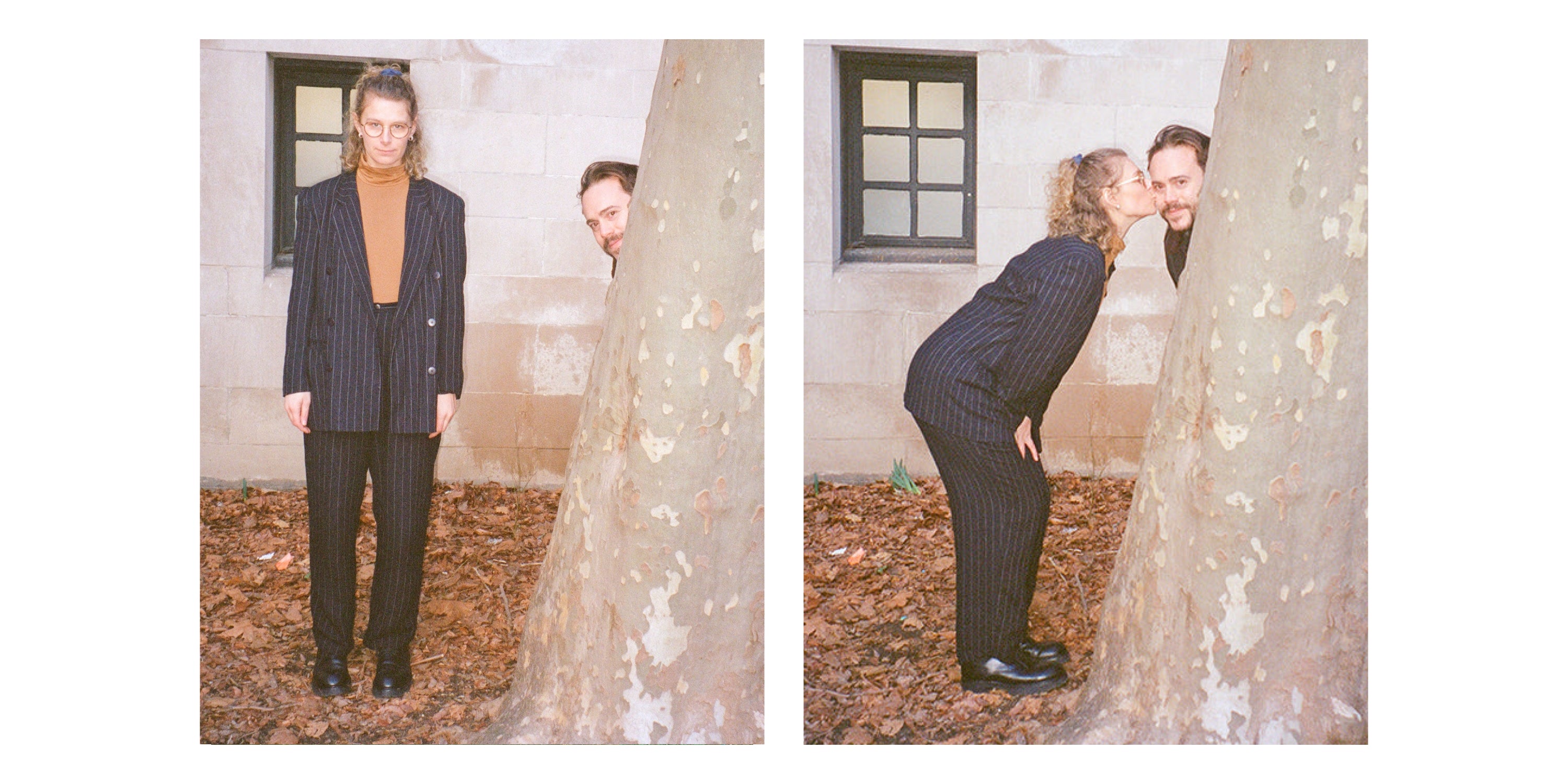 Mae and Kalen: two frames by a white brick building with a black window and dried leaves. Kalen peeks from behind a tree; Mae, next to the tree, wears a pinstripe suit and an orange JAS Mockneck.