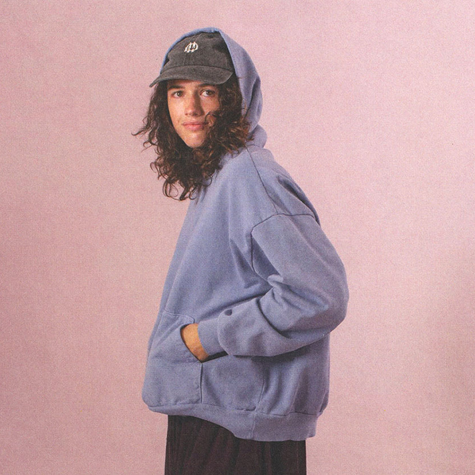 Person wearing a Periwinkle Trash Hoodie with the hood pulled up over a Bucky Logo Cap and Mulberry Tubular Pants.