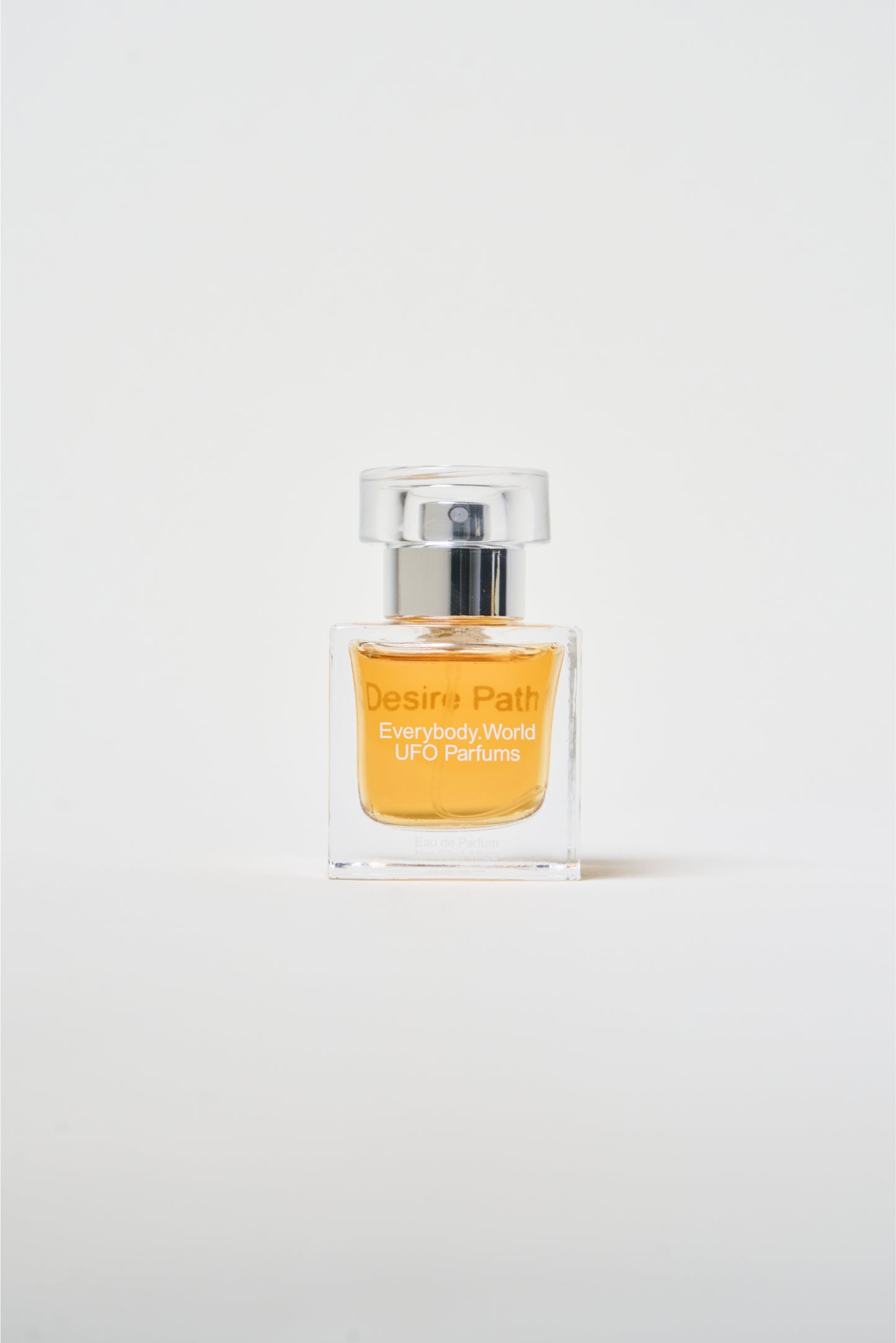 A clear glass bottle of Desire Path Eau de Parfum with a silver cap, containing a yellow-colored liquid.