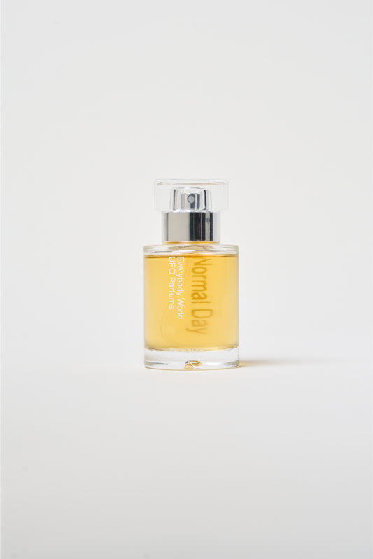 A clear glass bottle of Normal Day with a silver cap, containing a yellow-colored liquid.