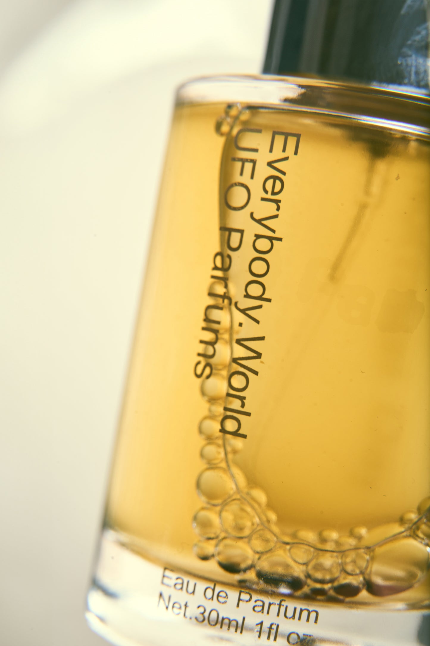 Close up of glass bottle printed with text "Everybody.World UFO Parfum" and volume info.
