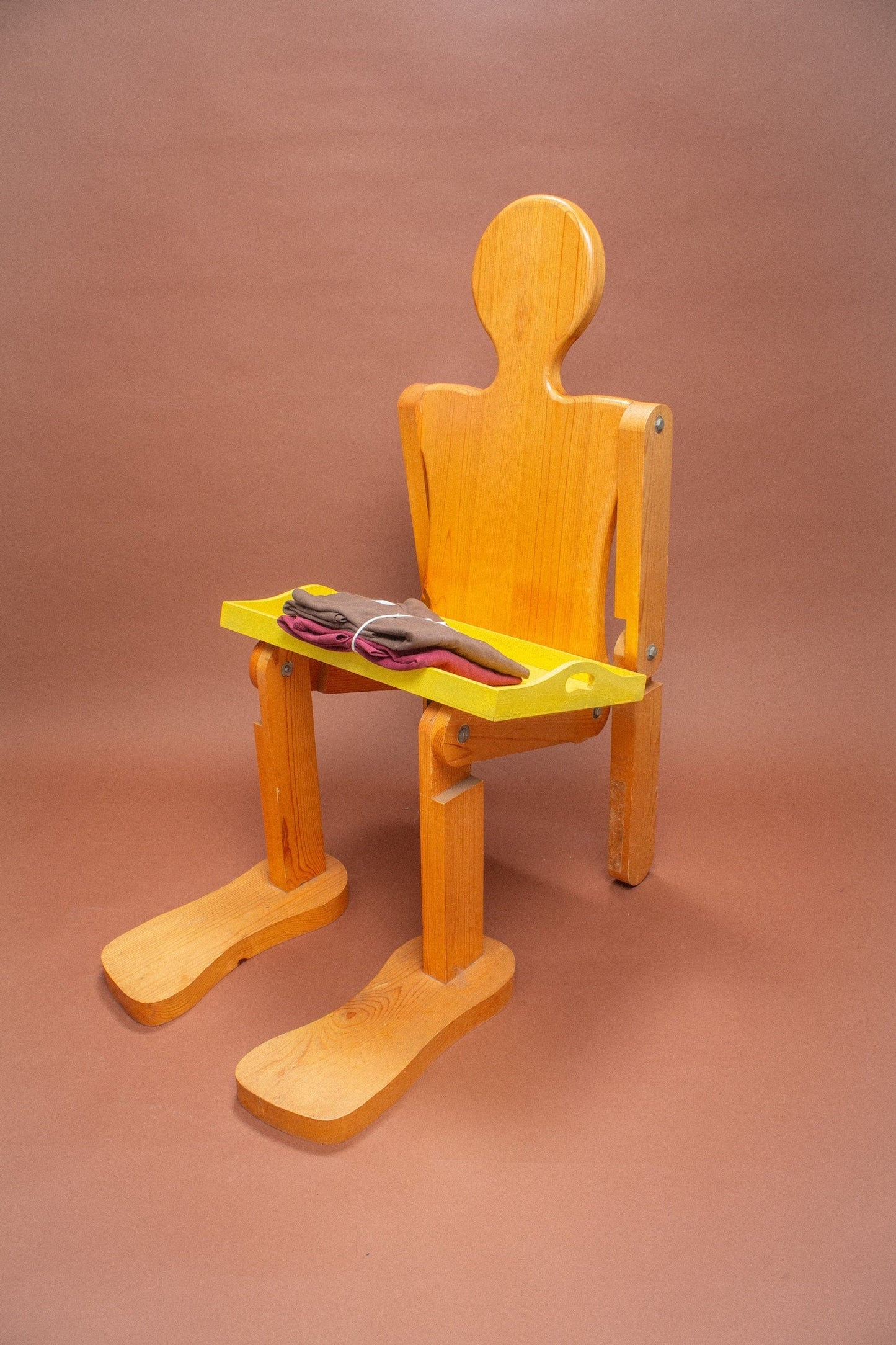 Wooden mannequin chair with Burgundy and Soil tees folded on its lap.