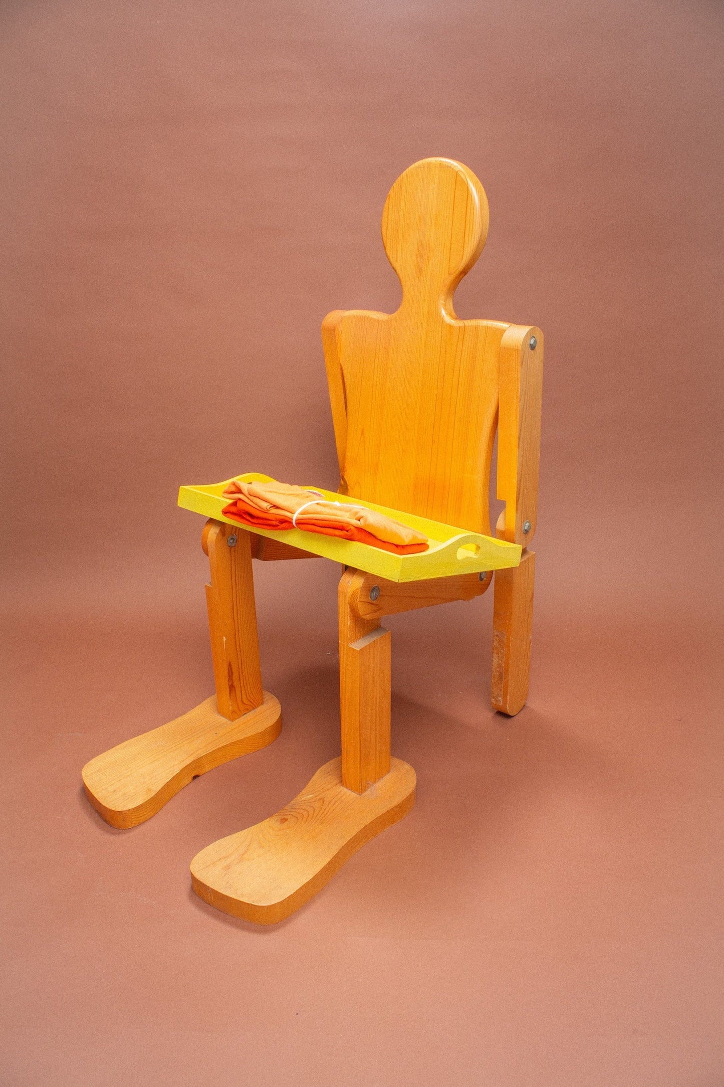 Wooden mannequin chair with peach and orange folded tees on it.