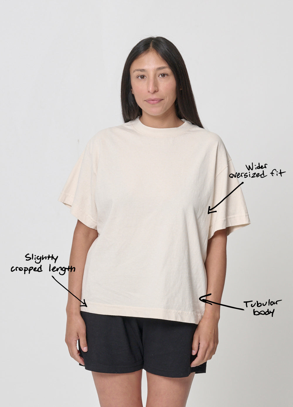 Woman wearing Boxier Trash Tee. Text overlay points to the upper mid-torso and says "wider relaxed fit," lower on the side of the shirt says "tubular body” and at the hem, "Slightly cropped length."