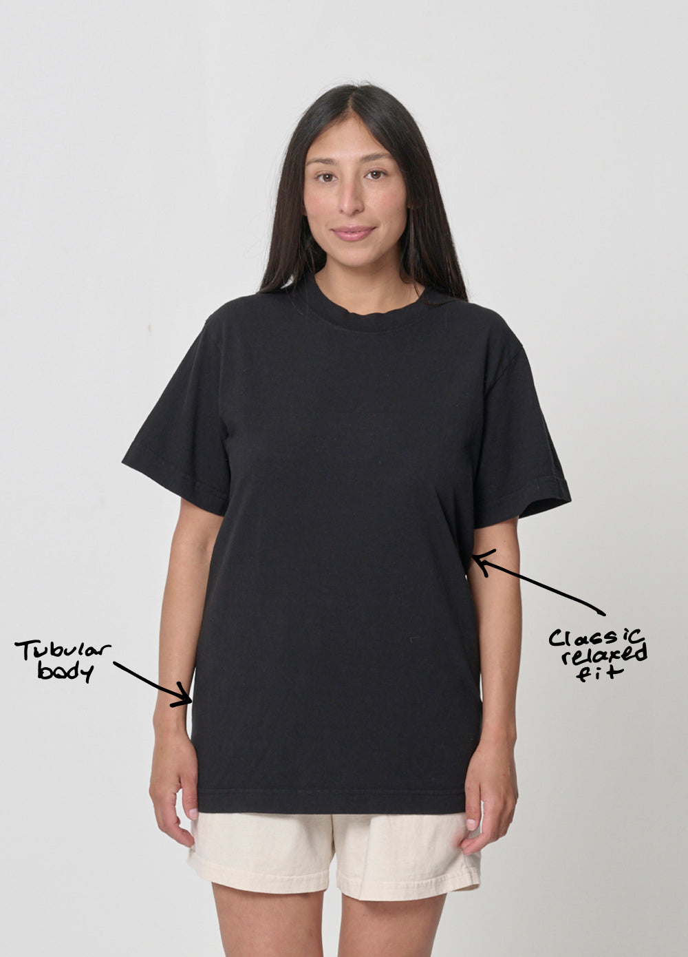 A person wearing a black t-shirt with label annotations, "classic relaxed fit" pointing to upper mid torso, and "tubular body" pointing at side of the shirt.