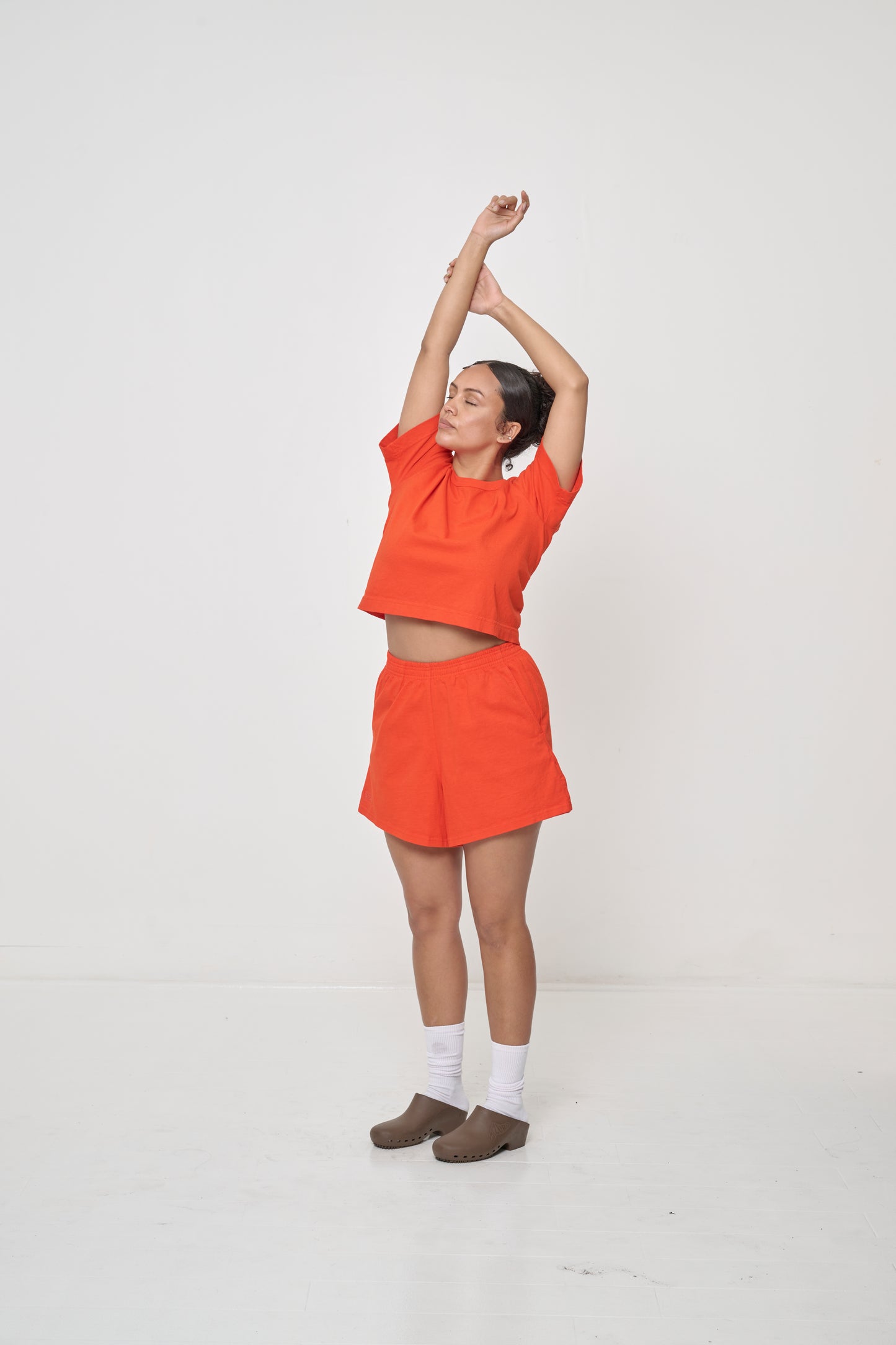 Full length of person, 3/4 angle, with arms reaching up and cropped shirt hem hits her mid-torso.