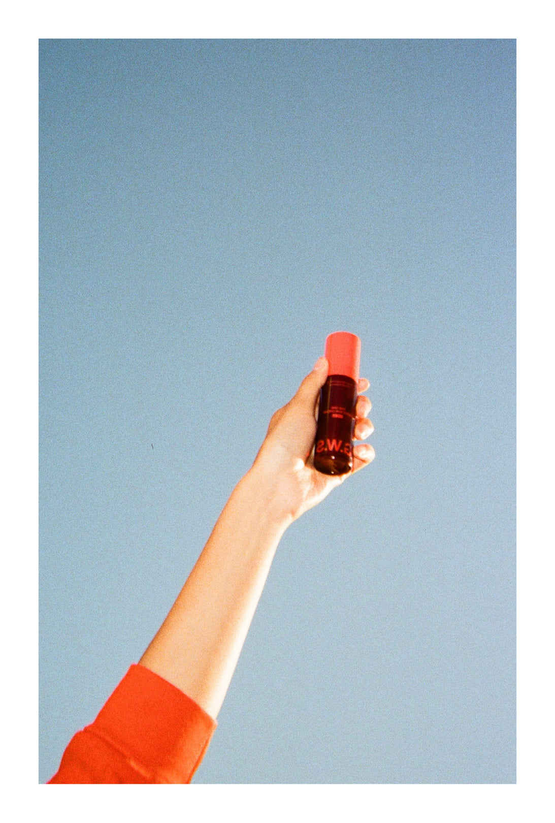 Hand holding a Good Weather Sun Cream bottle against blue sky.