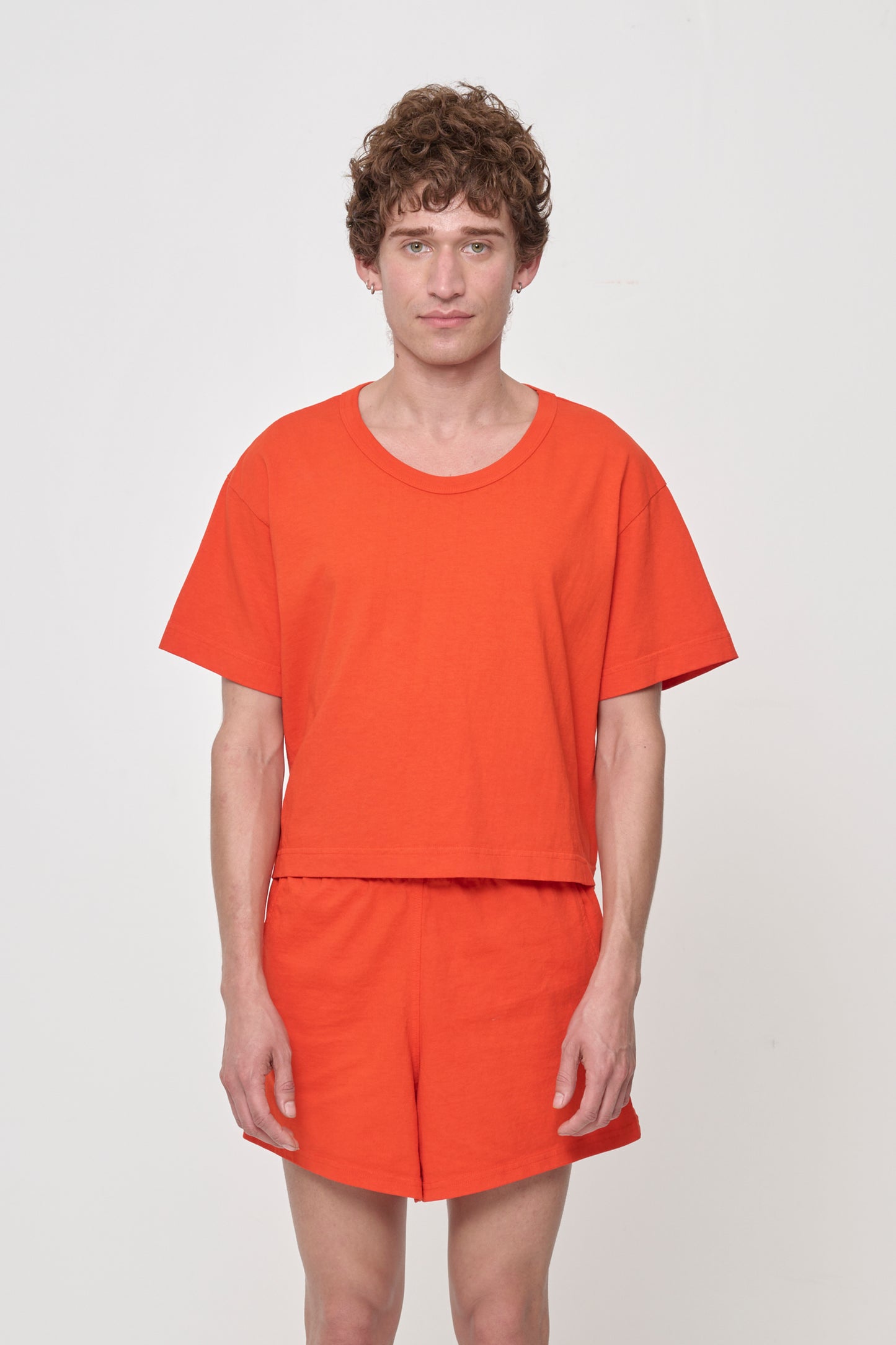 Close up of a person wearing a Hot Orange Good Weather Trash Tee, which is a cropped, boxy T-shirt with a scoop neckline and rib binding, paired with matching shorts.