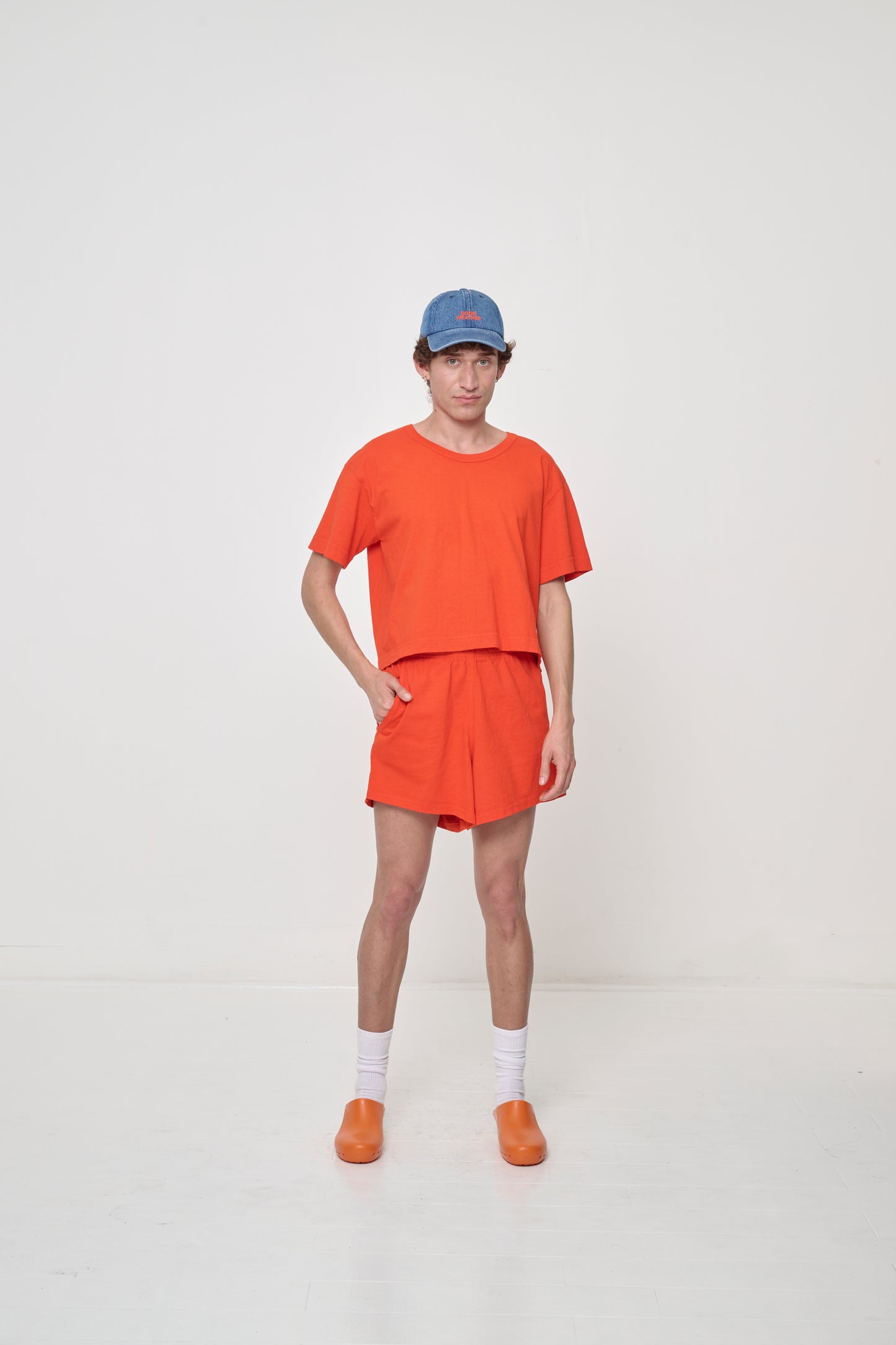 Full length front view of person, wearing Hot Orange Good Weather Trash Tee with matching shorts, with hand in side shorts pocket.