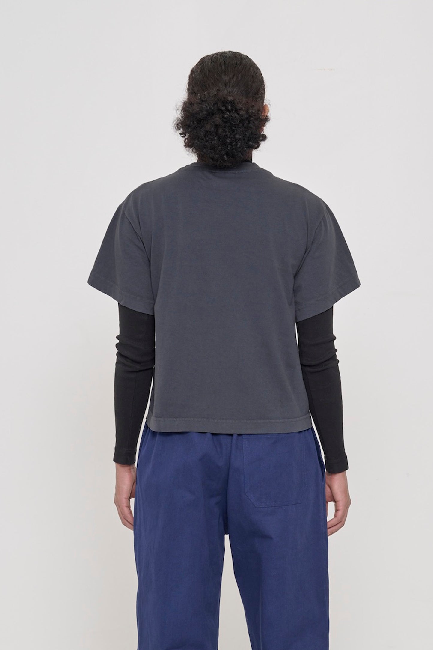 Back view of woman wearing Slate Heavyweight Boxier Trash Tee showing fabric drape and relaxed fit throughout.