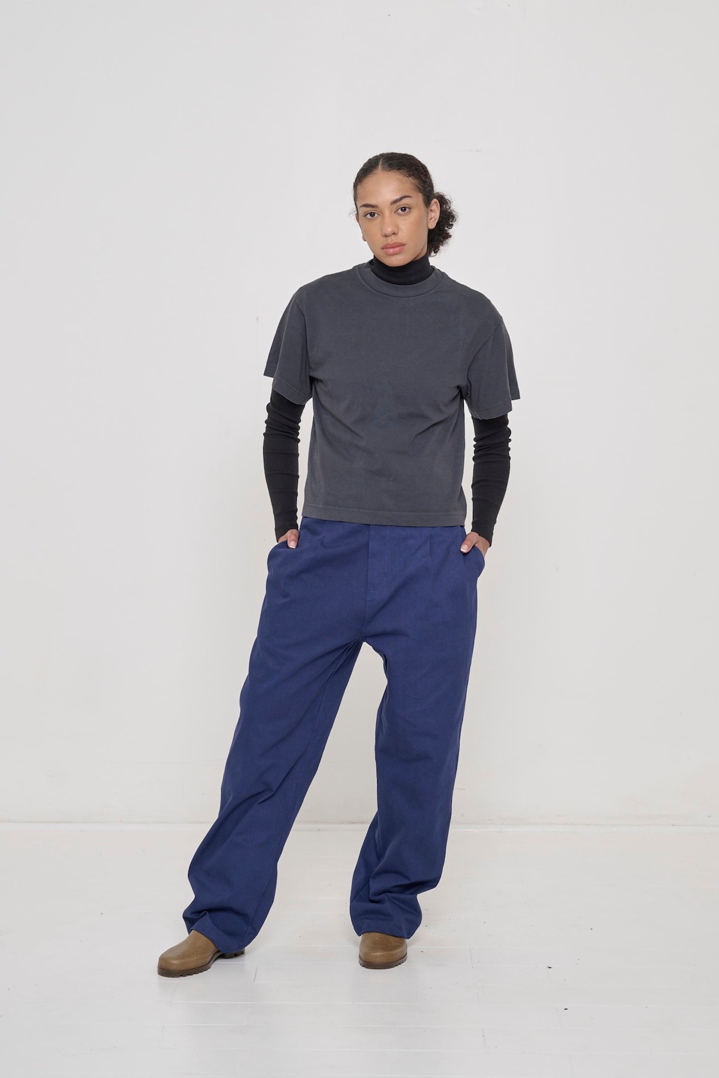 Woman in Slate Heavyweight Boxier Trash Tee over a Black Rib Turtleneck, hands in Cotton Twill Life Uniform Pants pockets.