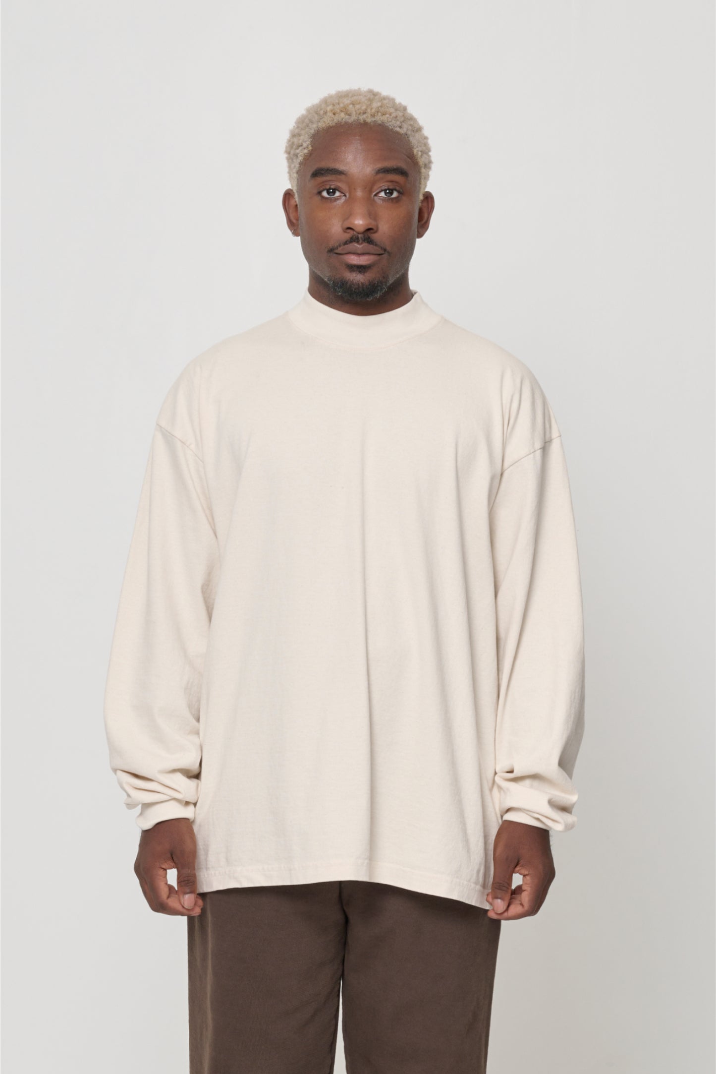 A person wearing a beige long-sleeve t-shirt with a rib knit mock neck collar, standing against a neutral background.