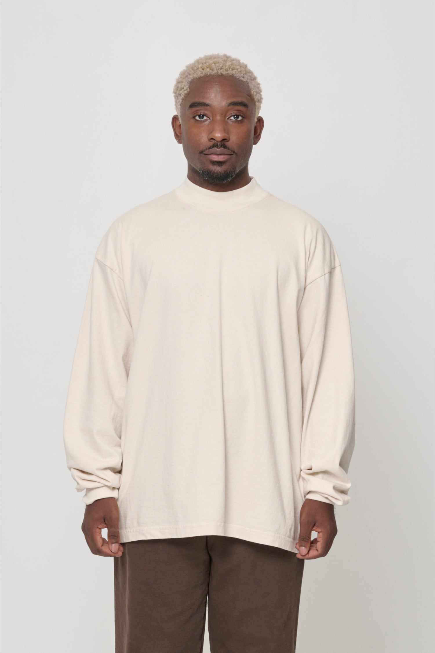 A person wearing a beige long-sleeve t-shirt with a rib knit mock neck collar