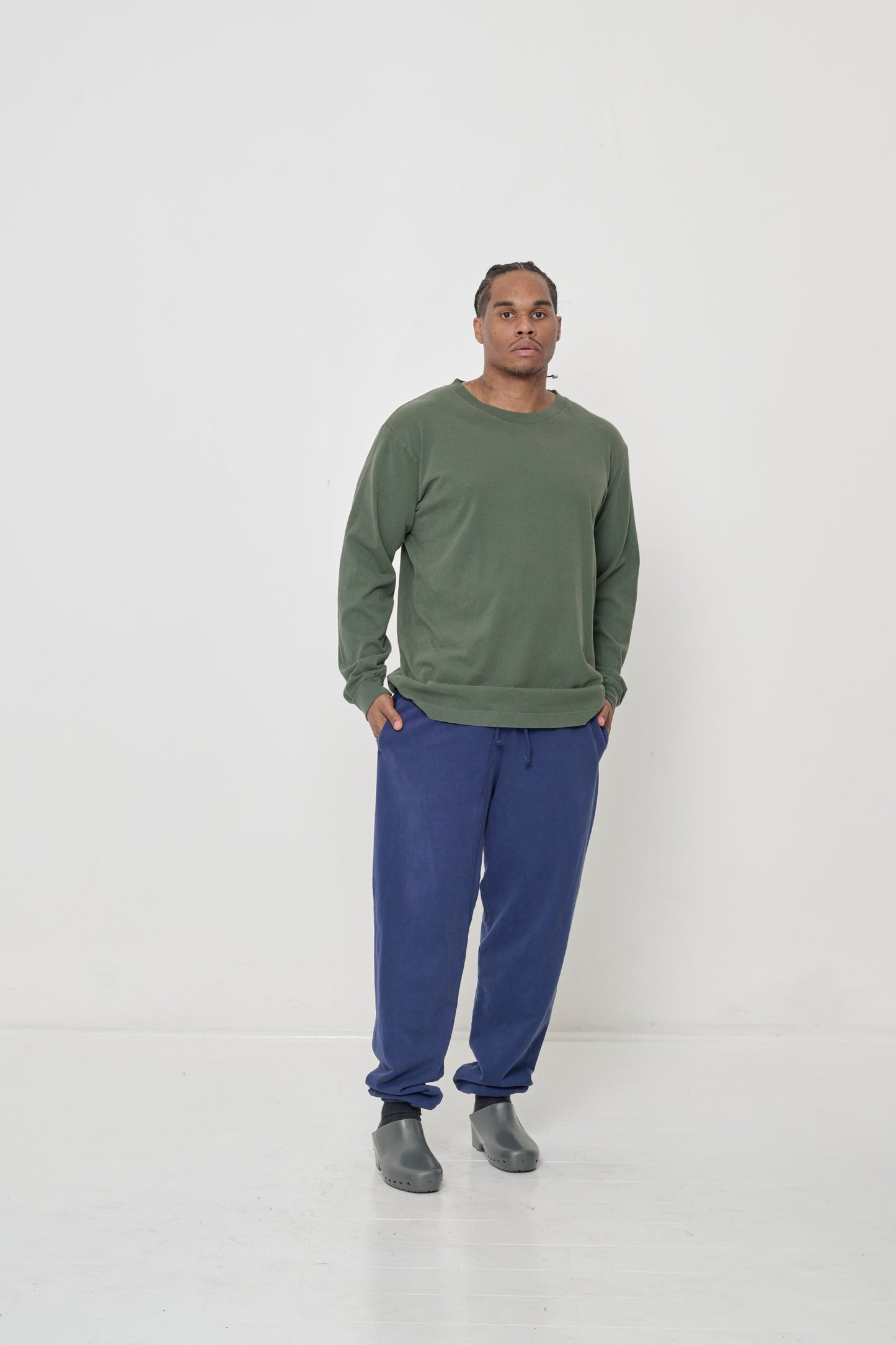 A man in a Pine Long Sleeve Trash Tee, with hands in Trash Sweatpants pocket, shows relaxed drape of shirt's sleeves.