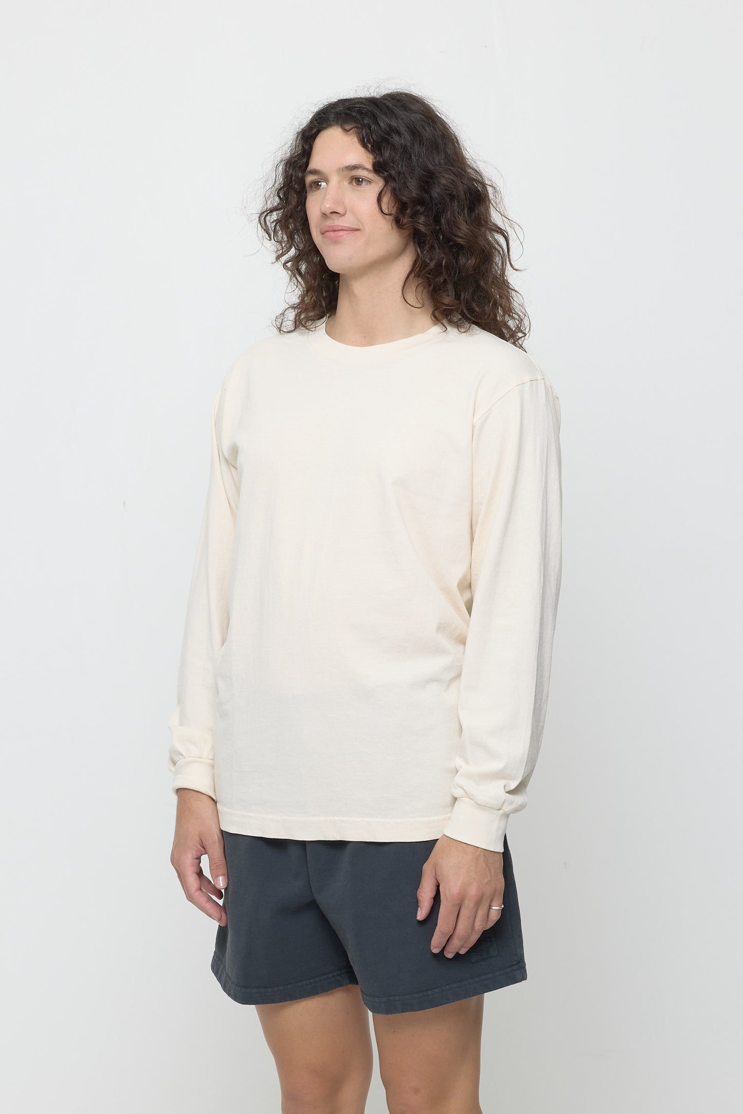 A person turned 45-degrees from the front, wearing a Scour Long Sleeve Trash Tee. Shows relaxed sleeves and rib cuff.